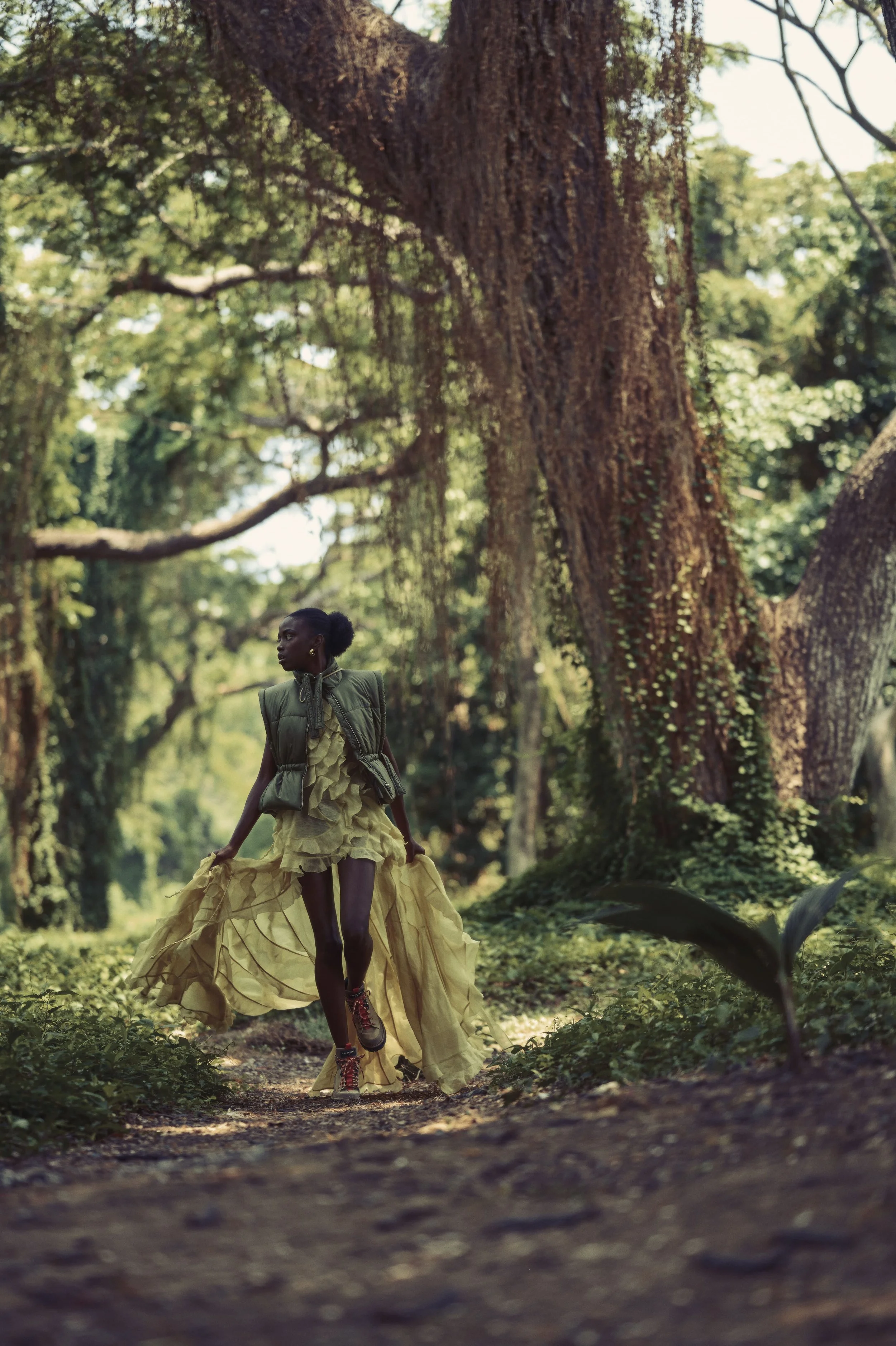 Vrouw in een groene jurk en vest loopt door een bos met grote bomen in Cuba gefotografeerd door Eric van den Elsen.