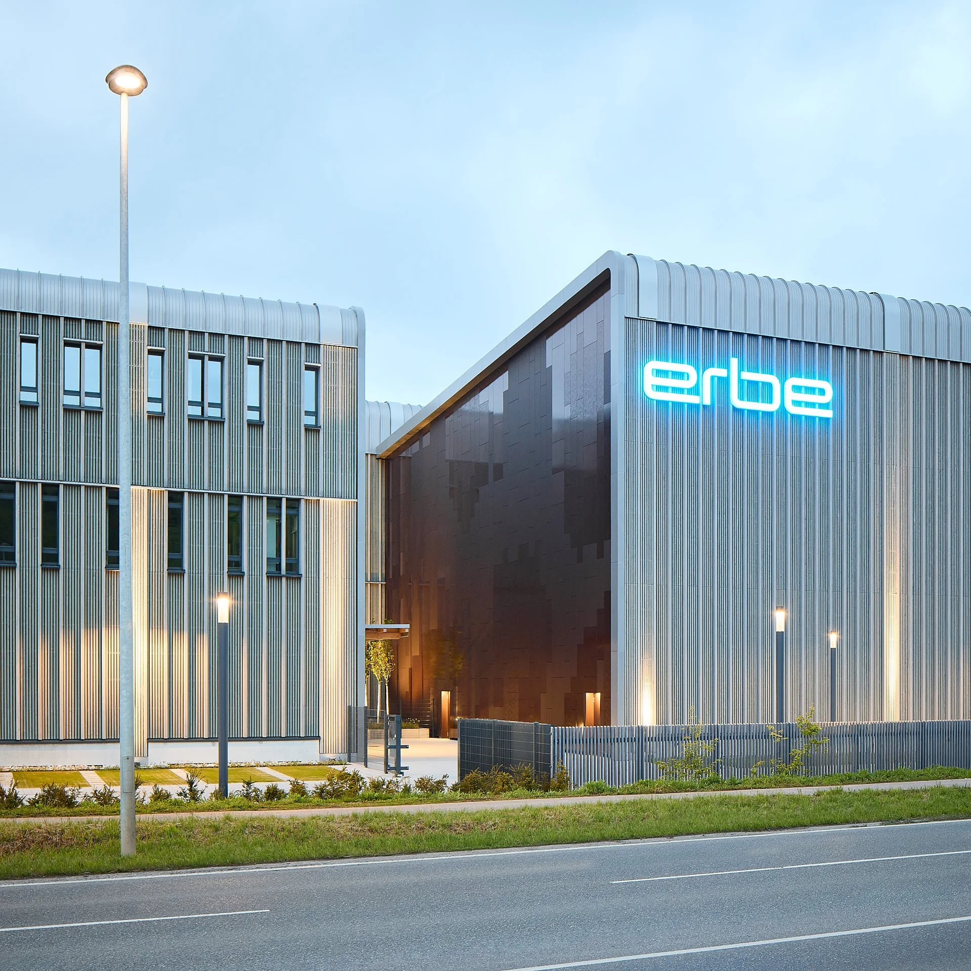 Abendliche Außenansicht des Erbe 4.i mit Holzfassade, Metallflächen und beleuchteten Bürobereichen