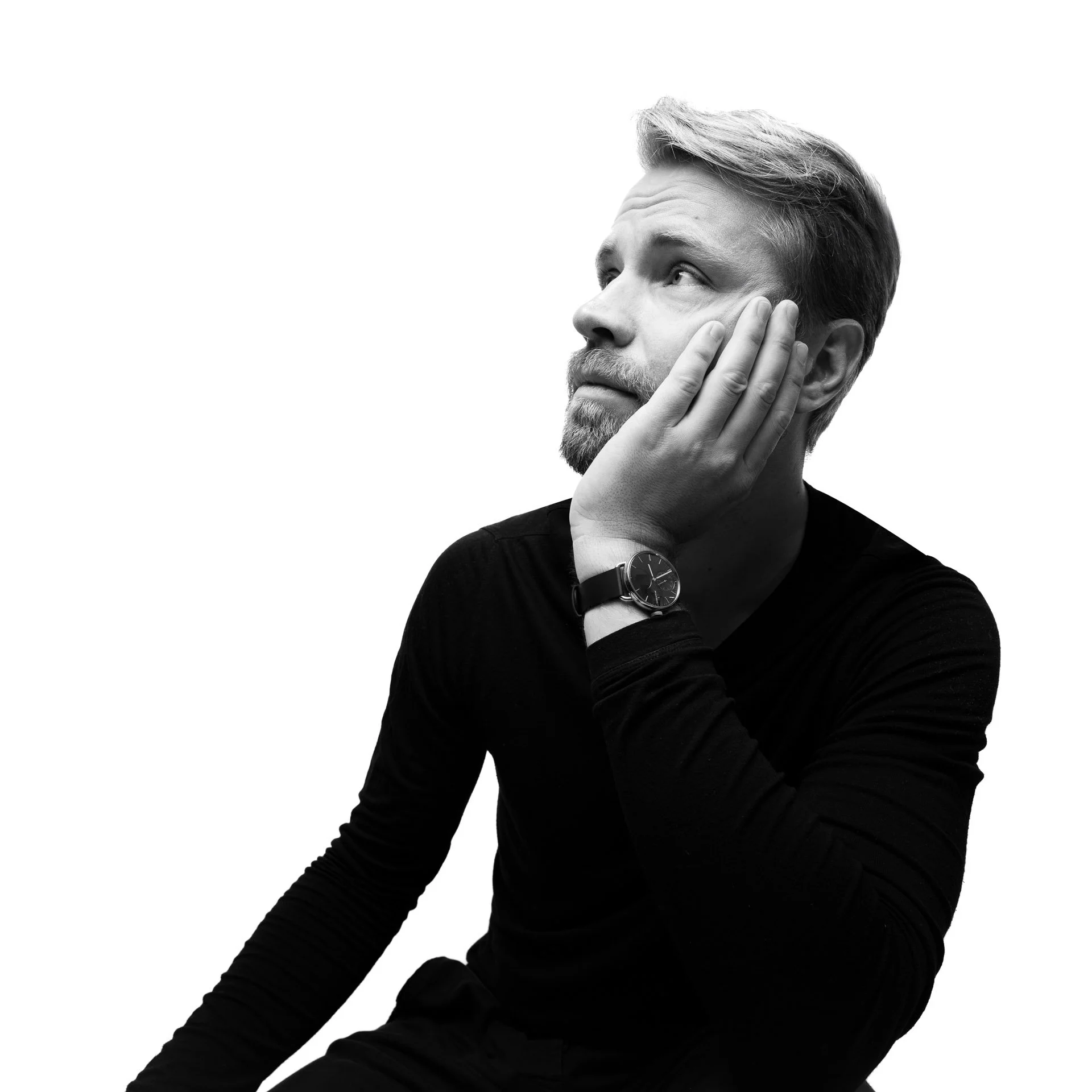 Black and white image of a pensive man supporting his cheek with his hand, wearing a black long-sleeved shirt and a wristwatch