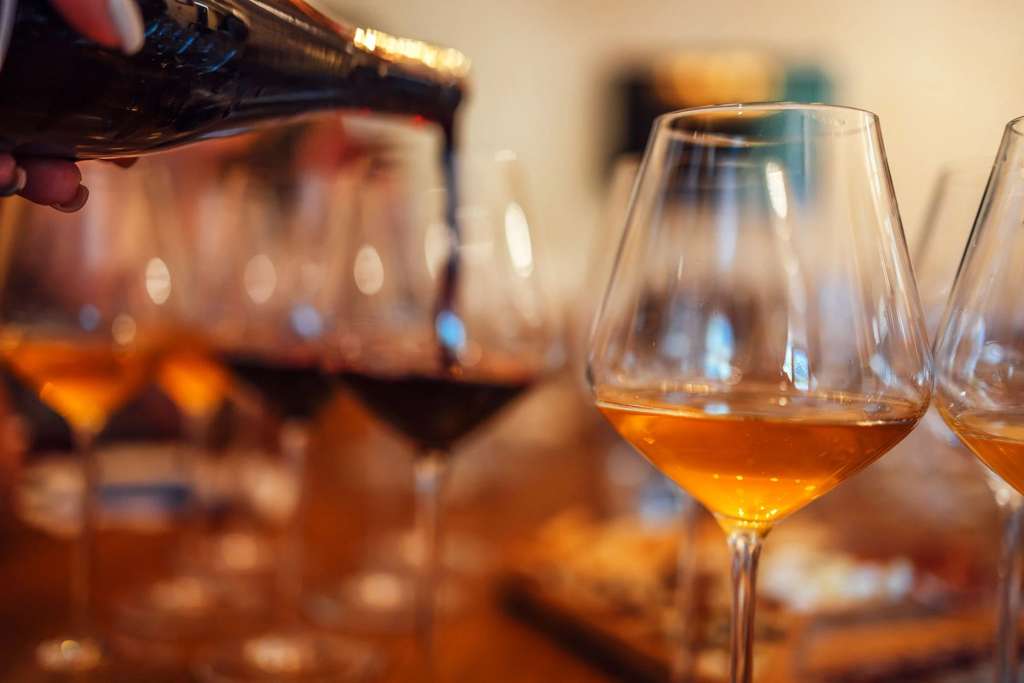 Several glasses of amber-colored alcohol, possibly whiskey or brandy, on a bar or table, with one glass being filled from a bottle.