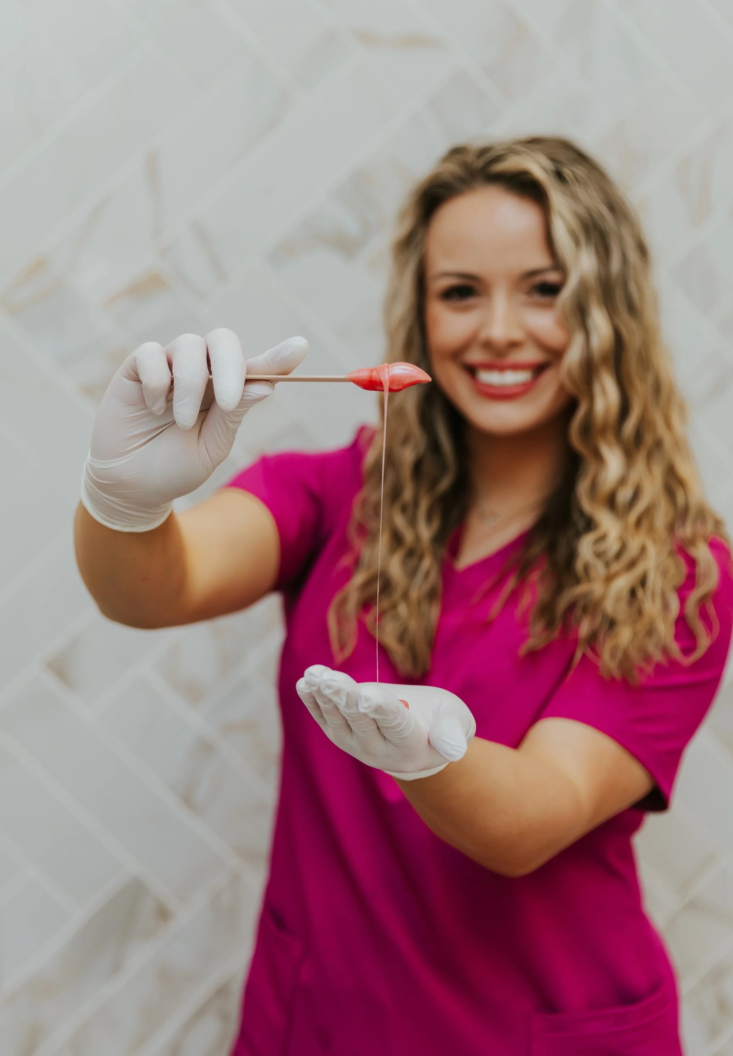 Aesthetician performing a facial treatment on a client using a handheld device, both wearing white. The aesthetician is wearing pink gloves.