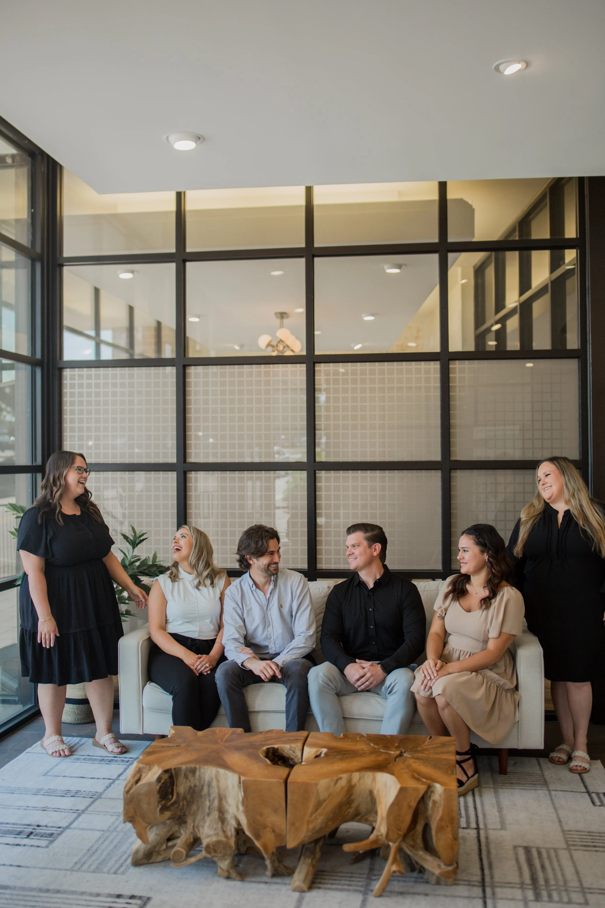 Group of five people in business attire sitting and standing around a modern table in an office setting.