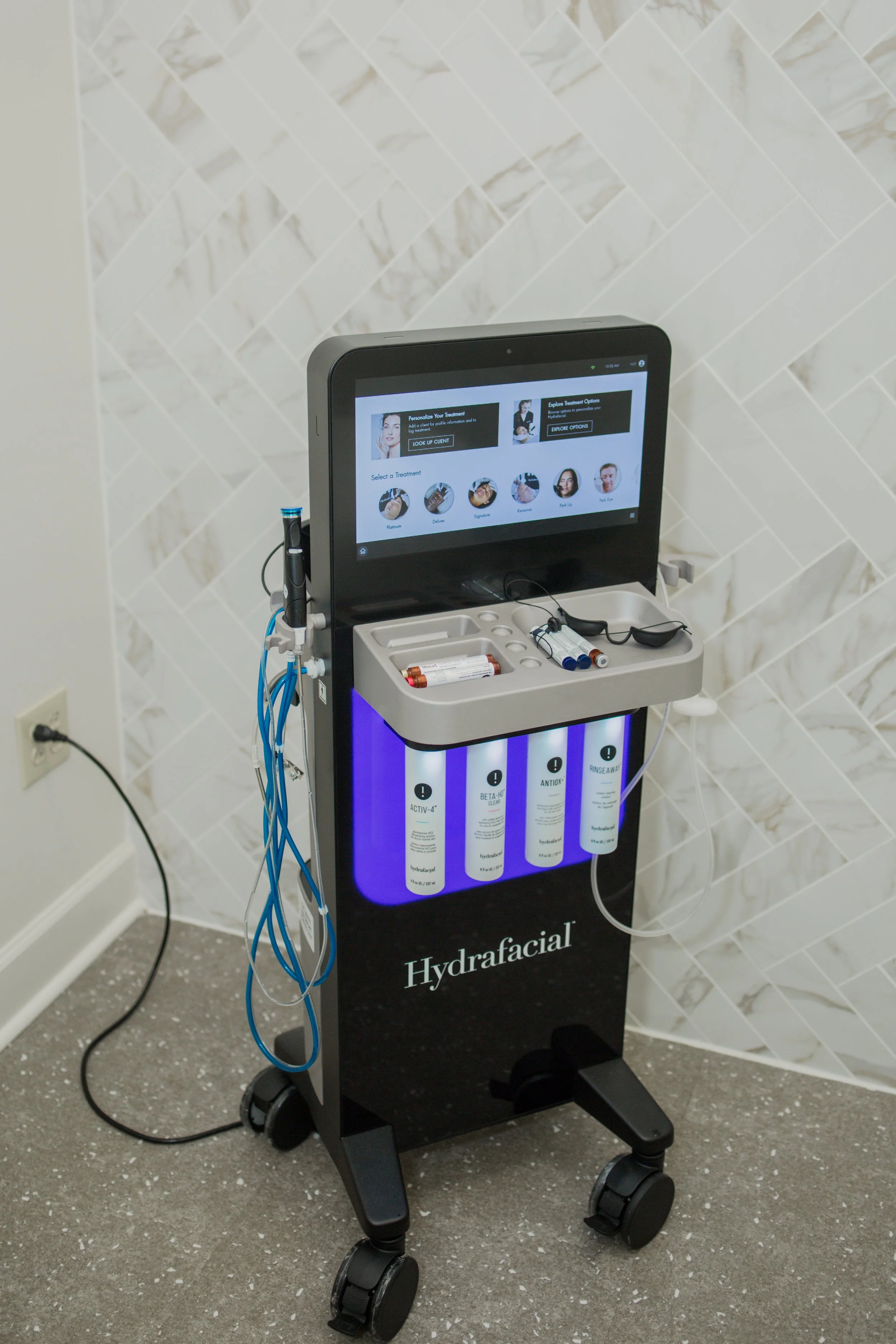 Hydrafacial machine with screen and skincare bottles in a clinic setting.