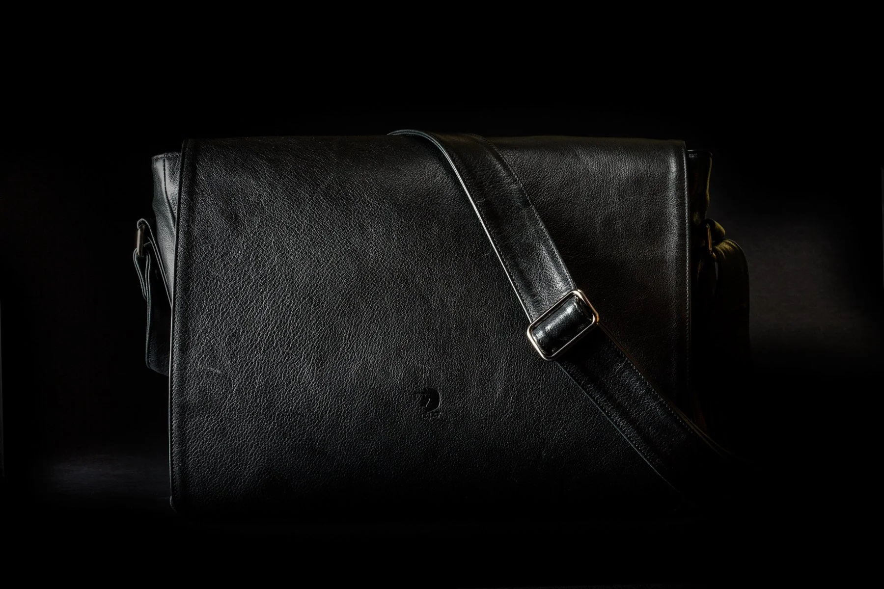 Borsa a tracolla nera in pelle su sfondo nero.