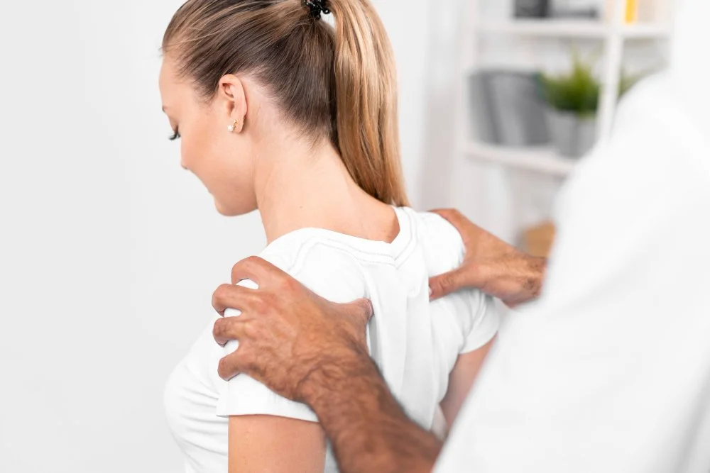 Doctor examining a young woman's shoulder in a clinical setting.