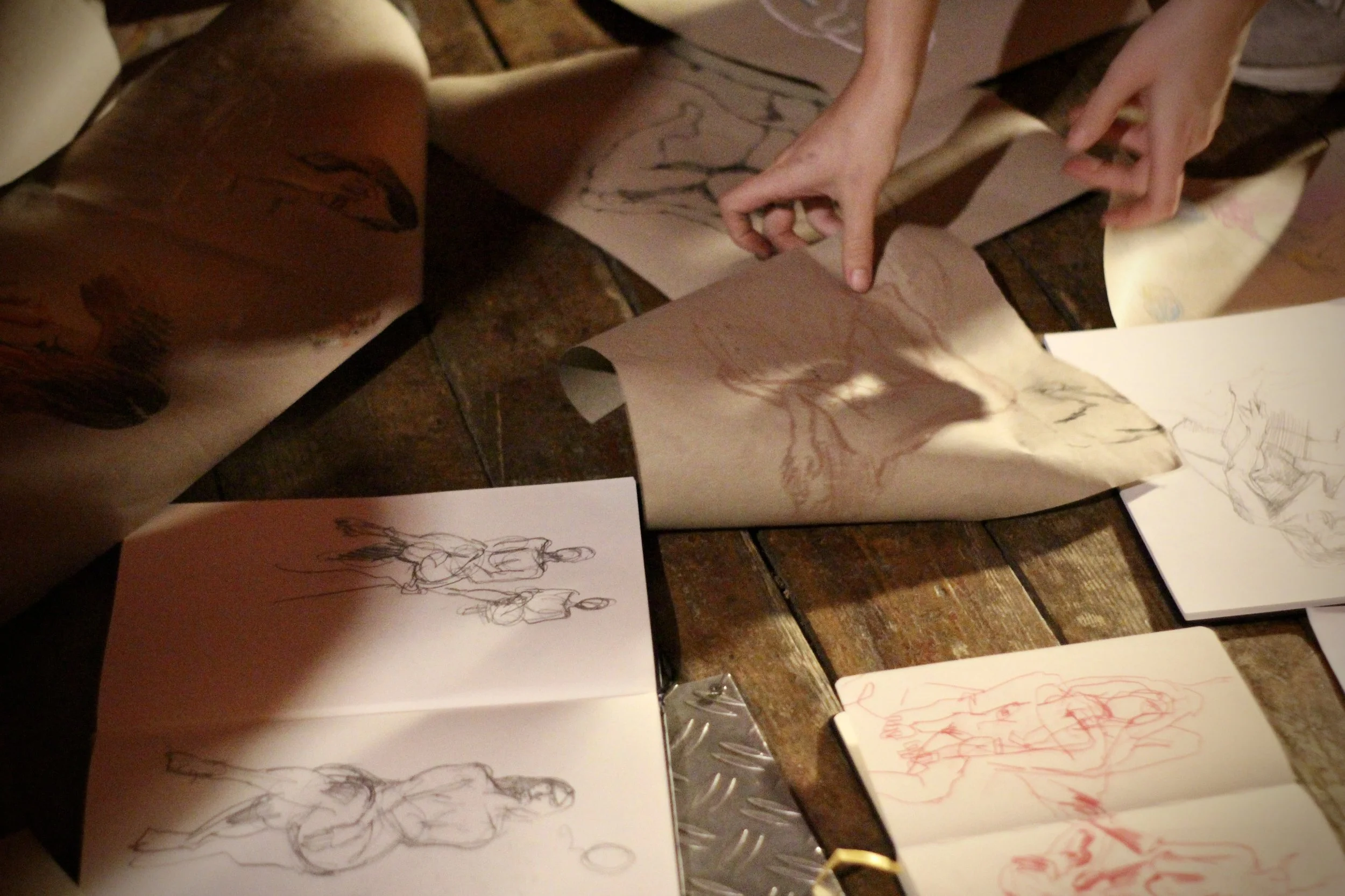 Personen, die Skizzen und Zeichnungen auf Papier erstellen, mit mehreren Skizzen auf Tischen aus Holz und Papier.