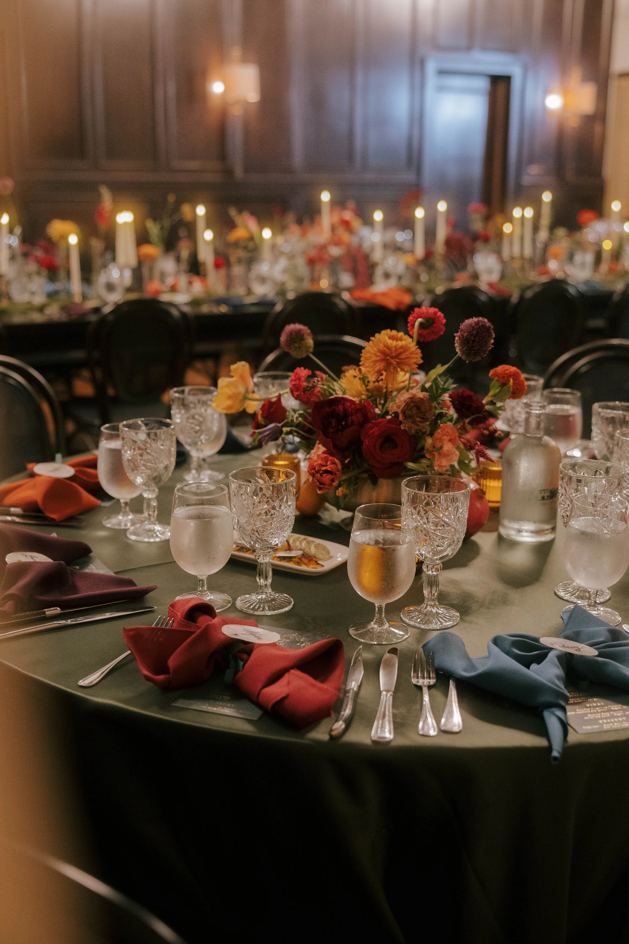 wedding reception table with centerpiece of dark jewel toned florals in a brass compote vase
