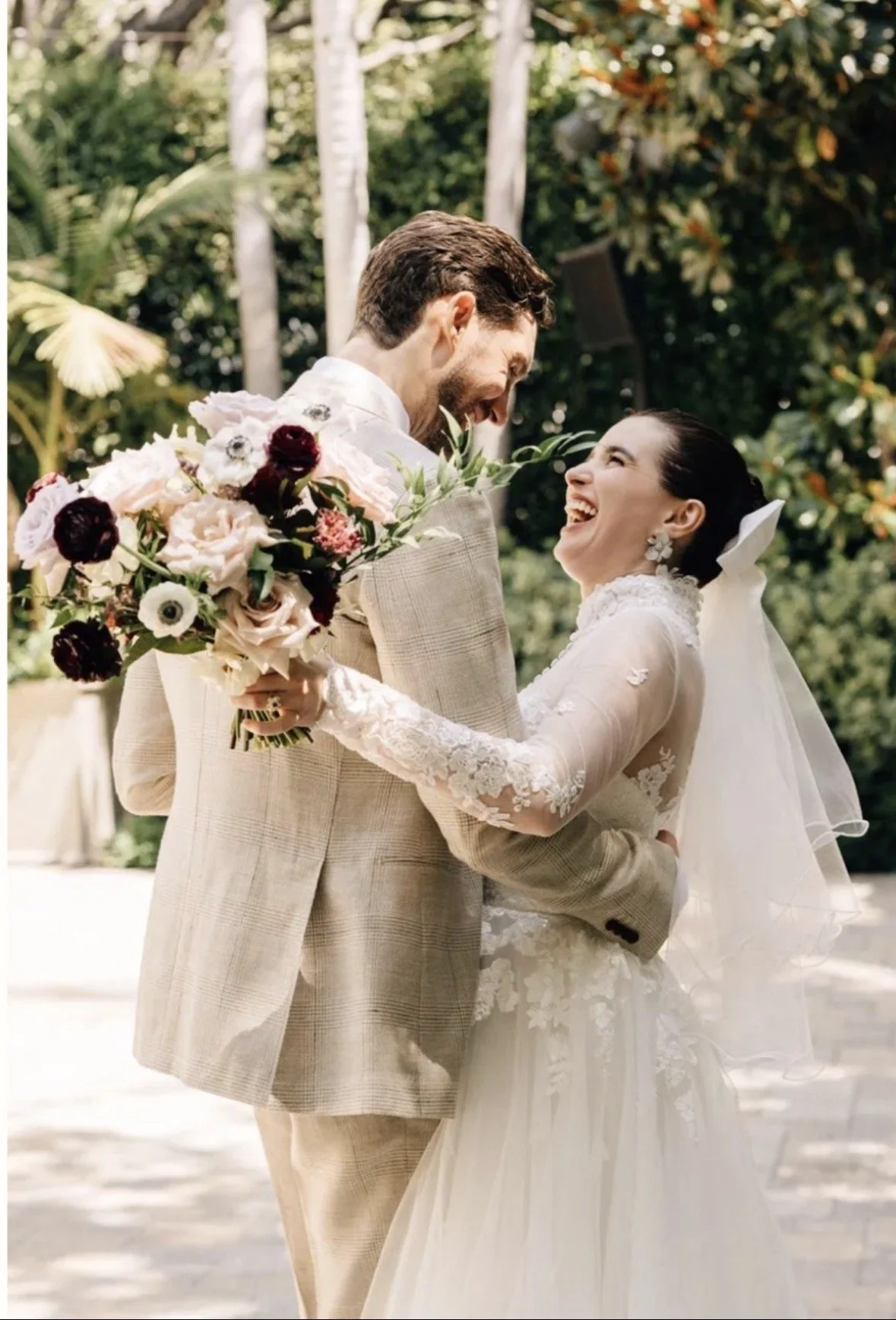 Newly married couple embracing and looking at each other smiling joyously. The bride holds her bouquet facing the camera. Bouquet is made up of white, blush, and burgundy florals.