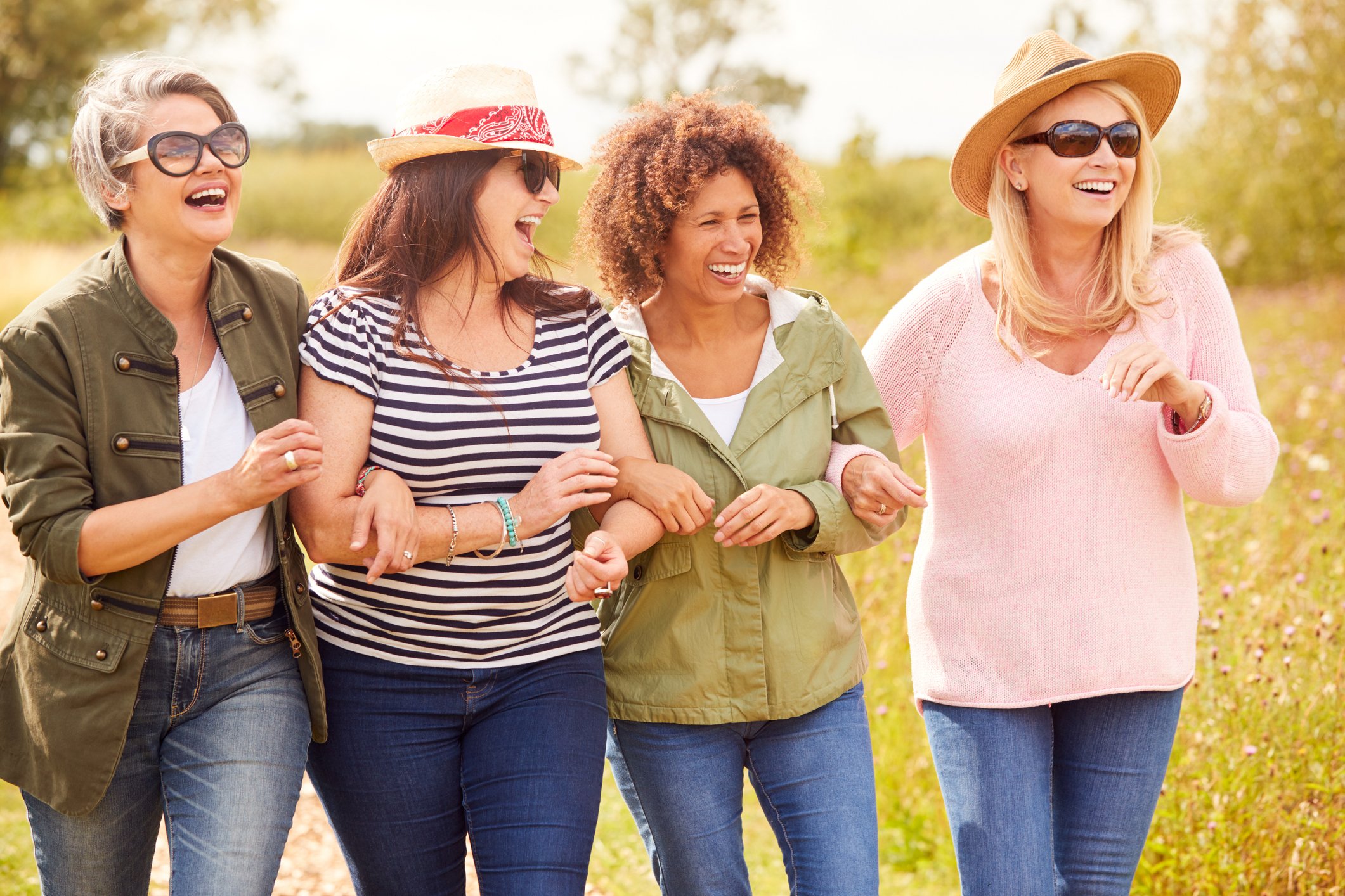 Four women walking outdoors in a sunny field, laughing and enjoying each other's company.