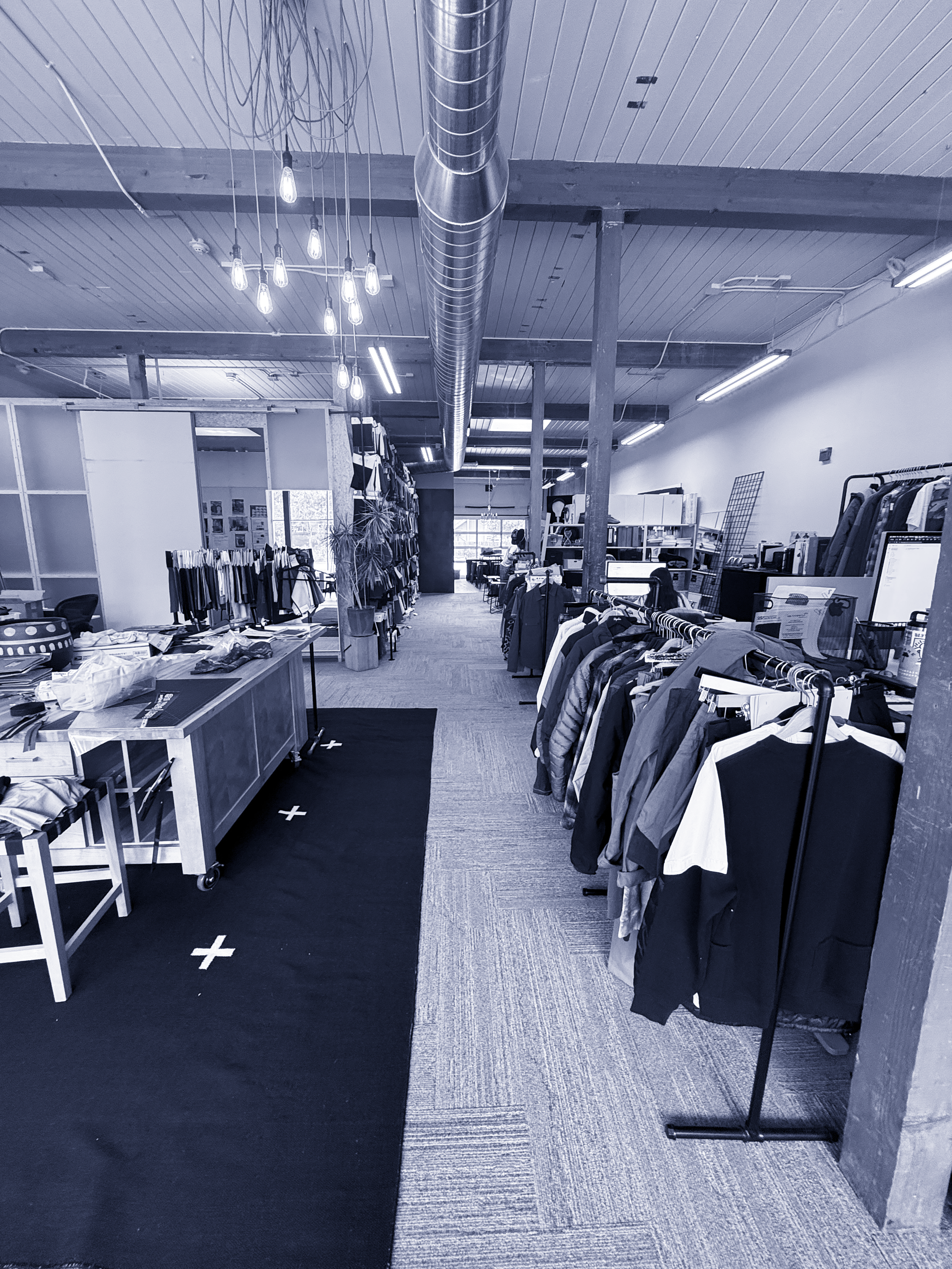 Inside an Sidfactor design studio  Ceiling features exposed ductwork and hanging Edison light bulbs. The store has a mix of carpet and tile flooring, with a black mat with white crosses near the entrance.