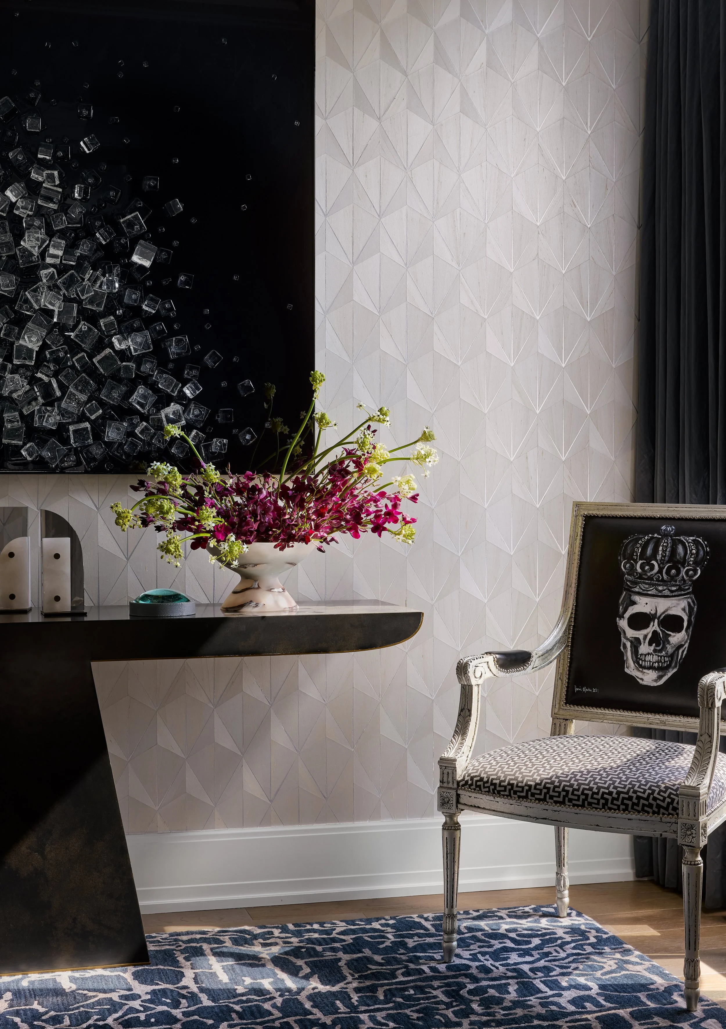 Luxury Lincoln Park condo foyer with artwork, subtle patterned wallpaper, an abstract floral arrangement, and chair with skull motif. A modern design by luxury interior design firm House of Mondi based in Chicago and Denver.