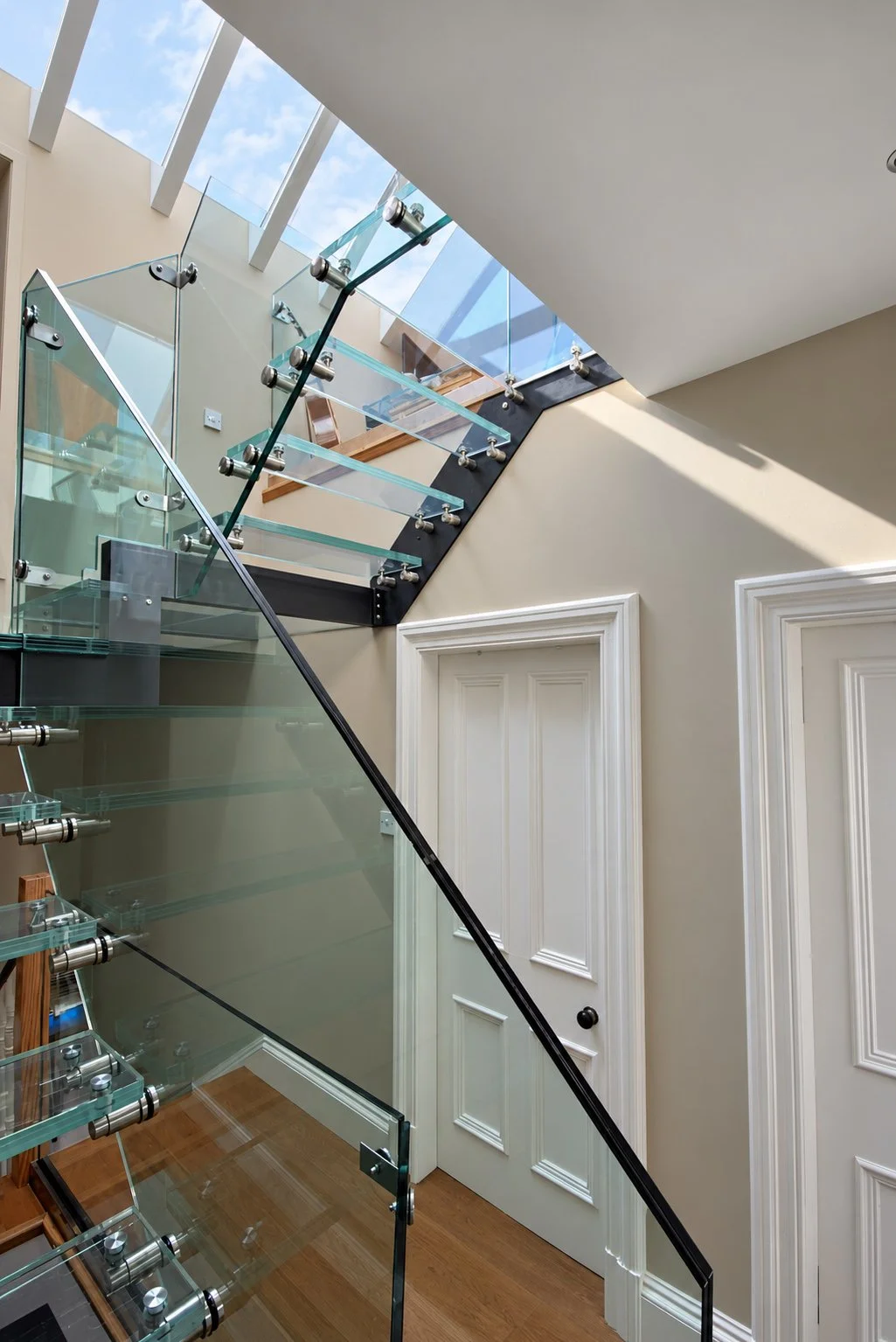 Upward view of a sculptural glass staircase rising towards roof glazing in a Newport-on-Tay loft conversion.