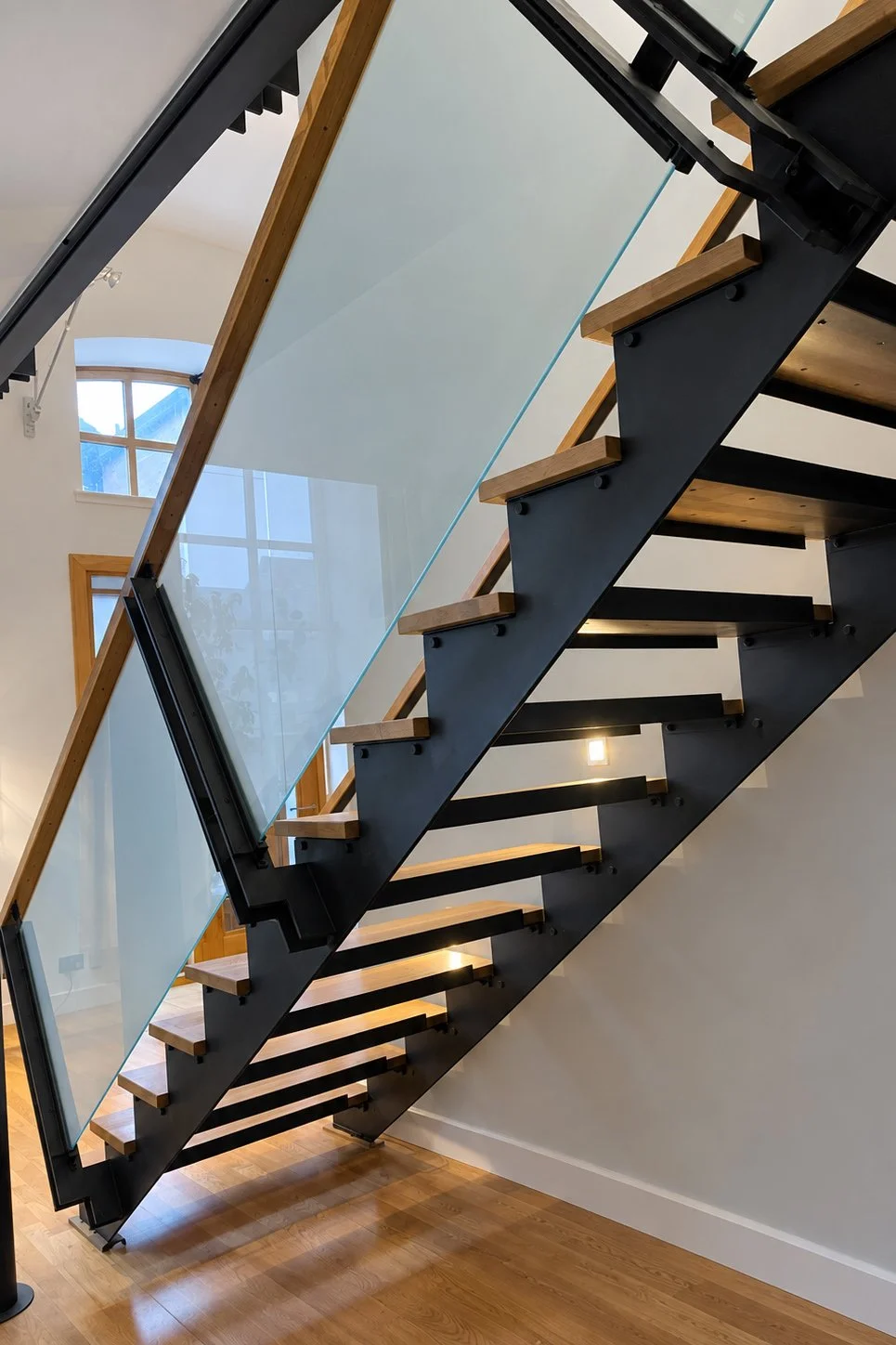 Bespoke black steel and oak staircase with frameless glass balustrade in the converted engine room.