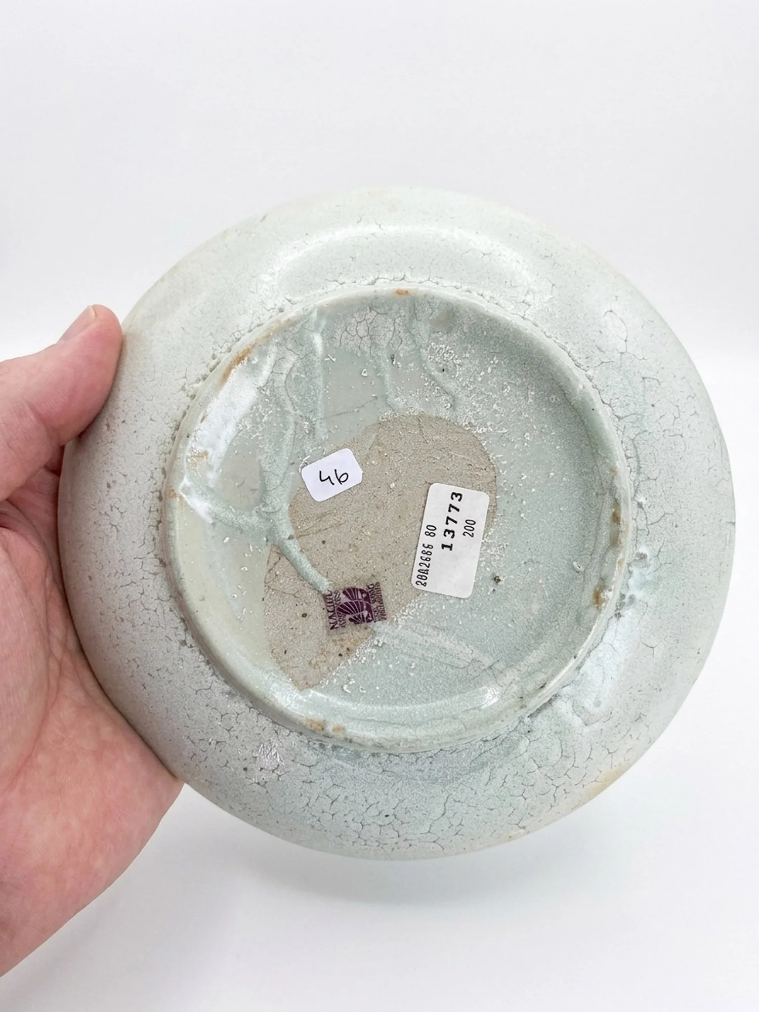 Underside of a Tek Sing shipwreck dish showing original Nagel Auctions salvage lot 13773 labels and heavy glaze craquelure.