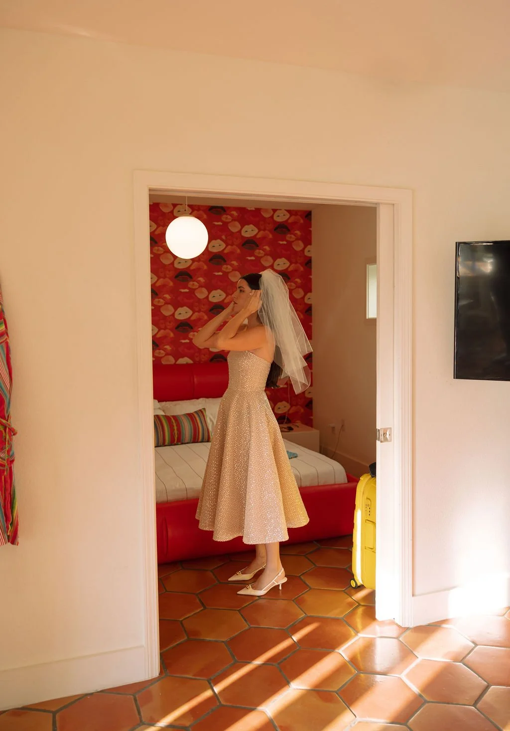 Stephanie adjusting her veil inside their Austin Motel suite with retro red wallpaper in the background