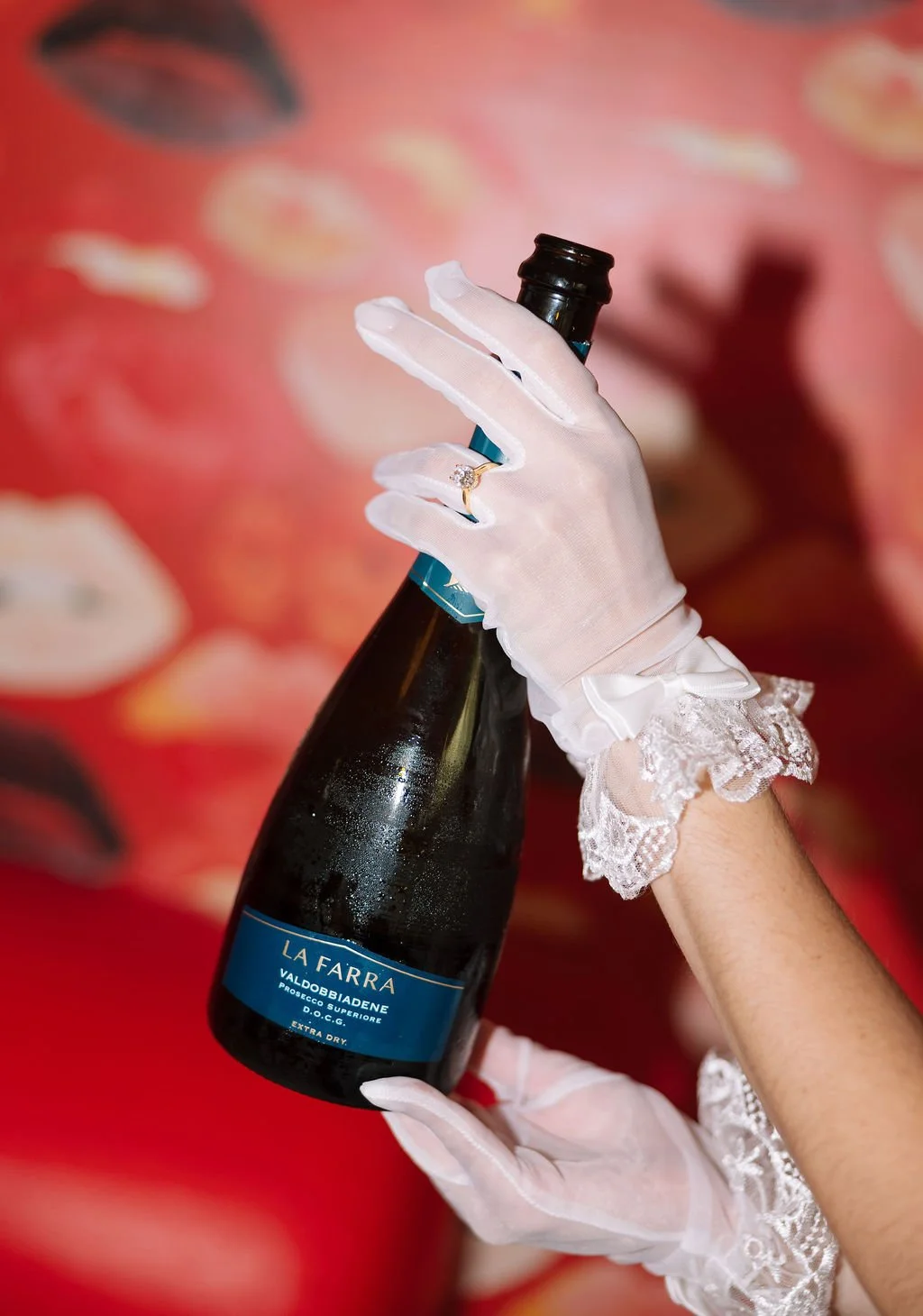 Close-up of Stephanie’s gloved hands holding champagne bottle against retro red wallpaper inside Austin Motel