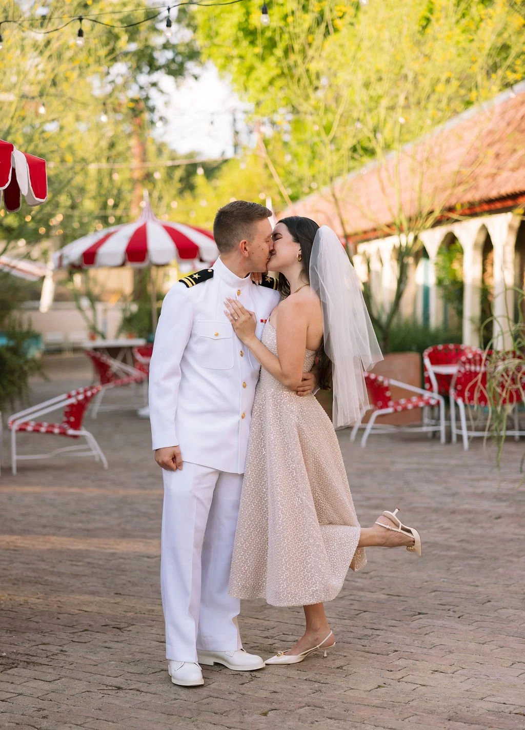 Couple kissing outside their Austin Motel suite with red patio chairs and umbrellas in background