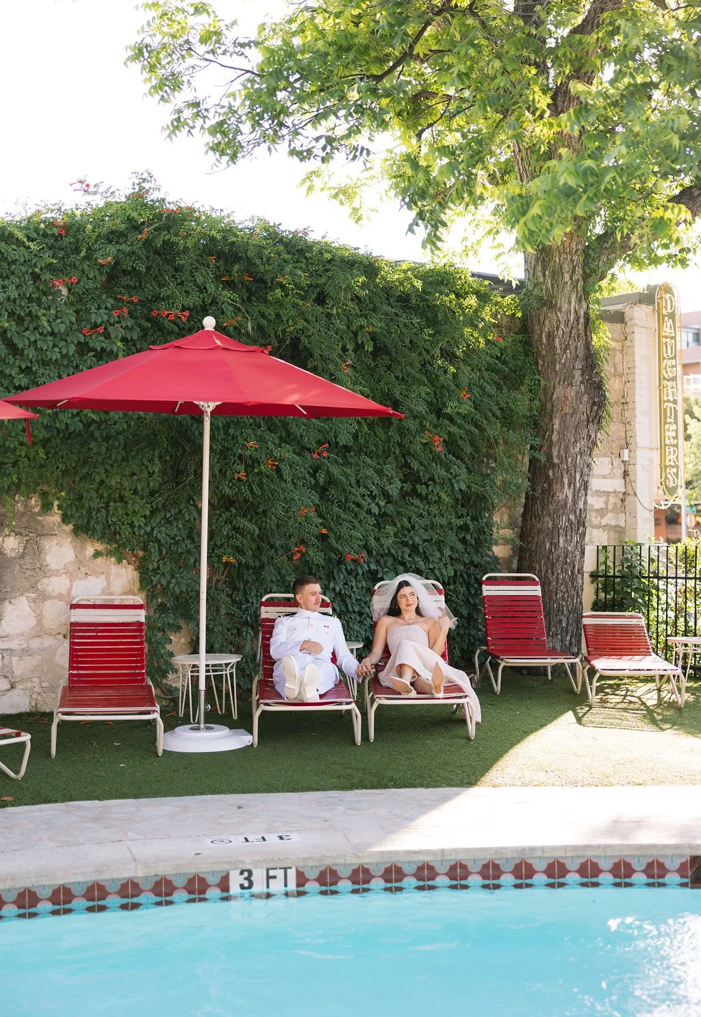 Couple lounging by retro-style pool at Austin Motel under red umbrellas