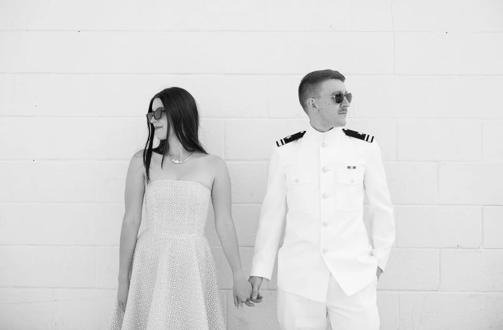 Black and white photo of couple holding hands against white brick wall on South Congress