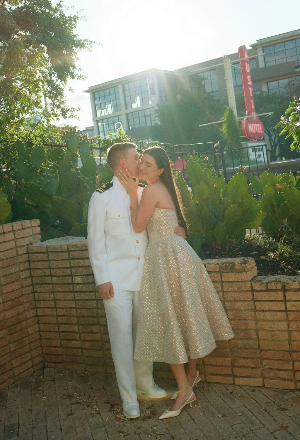 Couple kissing against brick wall with Austin Motel sign in background on fuji film