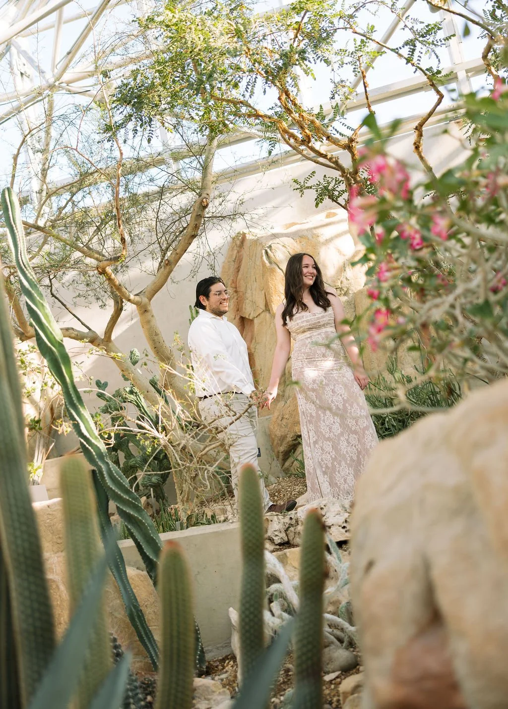 Couple walking hand in hand through desert plants at San Antonio Botanical Garden engagement session.