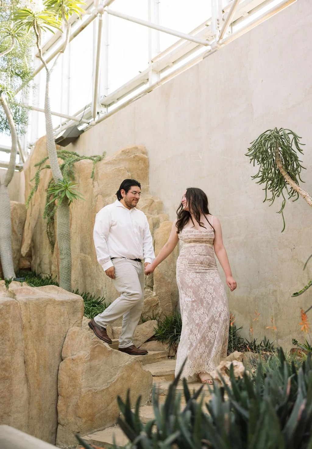 Couple smiling and holding hands on stone steps surrounded by greenery at San Antonio Botanical Garden.