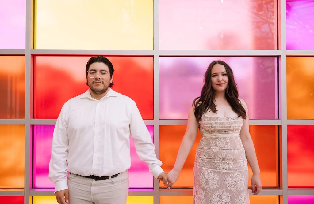 Couple smiling in front of rainbow wall during San Antonio engagement session at Botanical Garden.