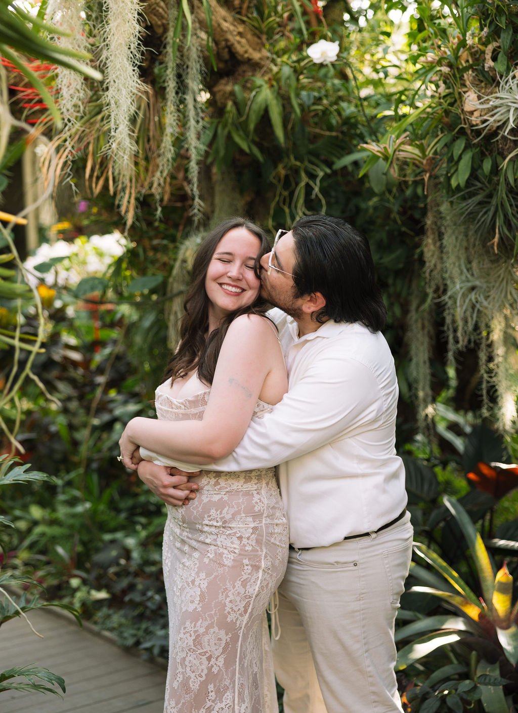 Couple hugging among lush tropical greenery at San Antonio Botanical Garden engagement photos.