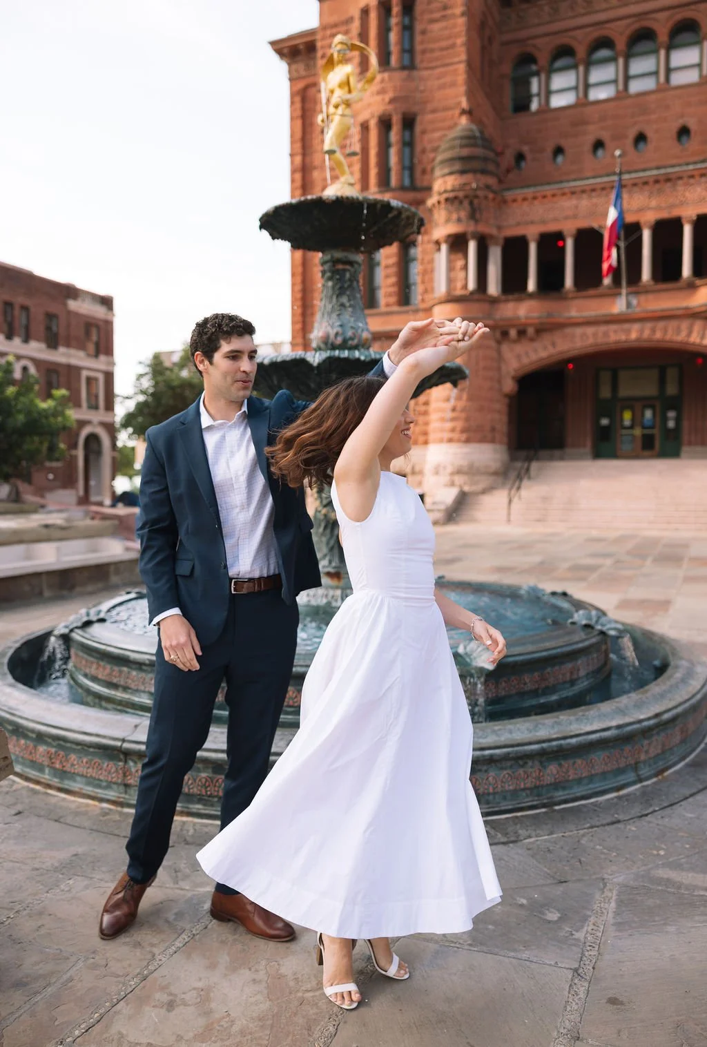 Couple dancing by fountain in front of historic building during engagement photos San Antonio.