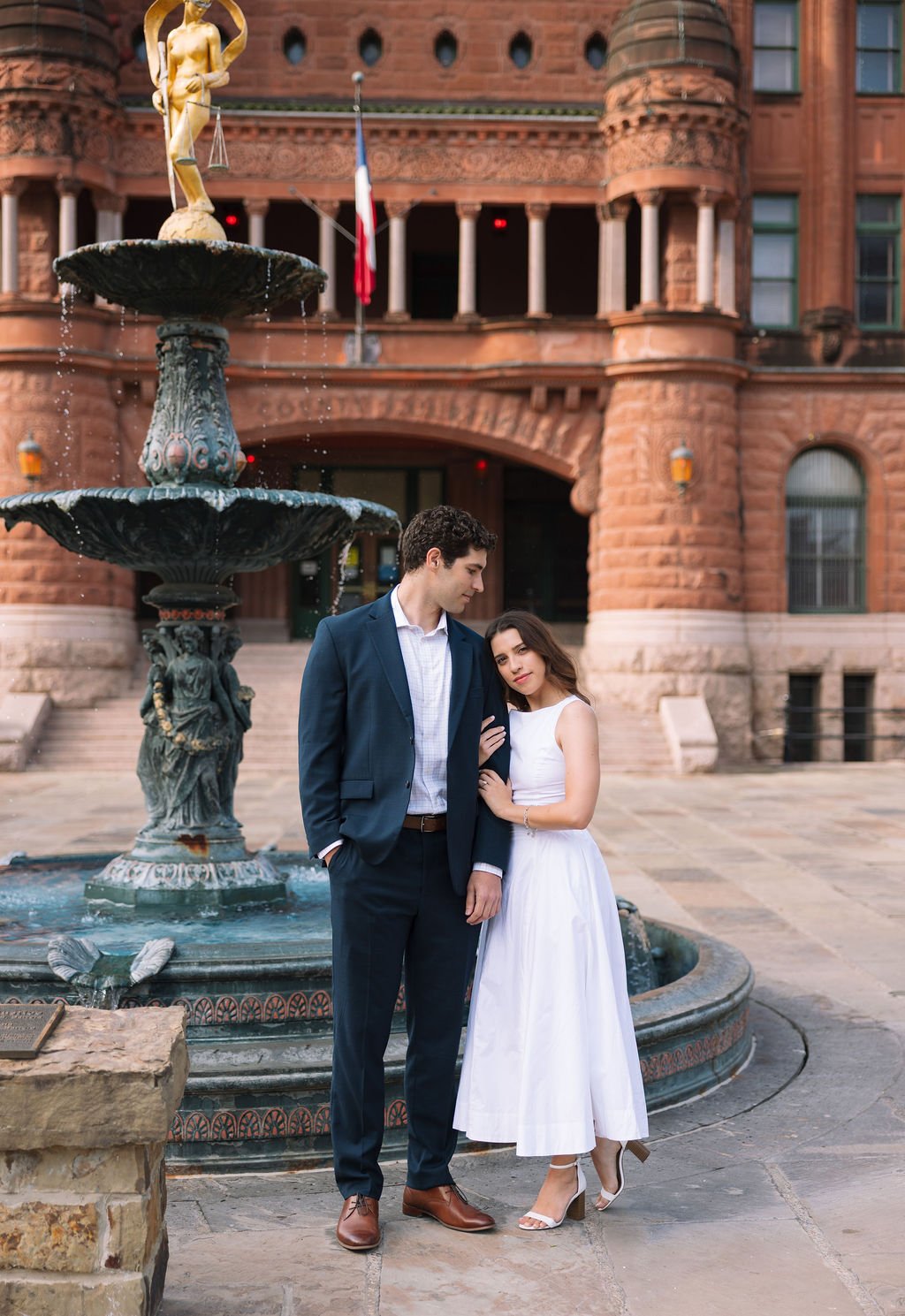 Couple standing close beside fountain with historic courthouse backdrop, engagement photos San Antonio.