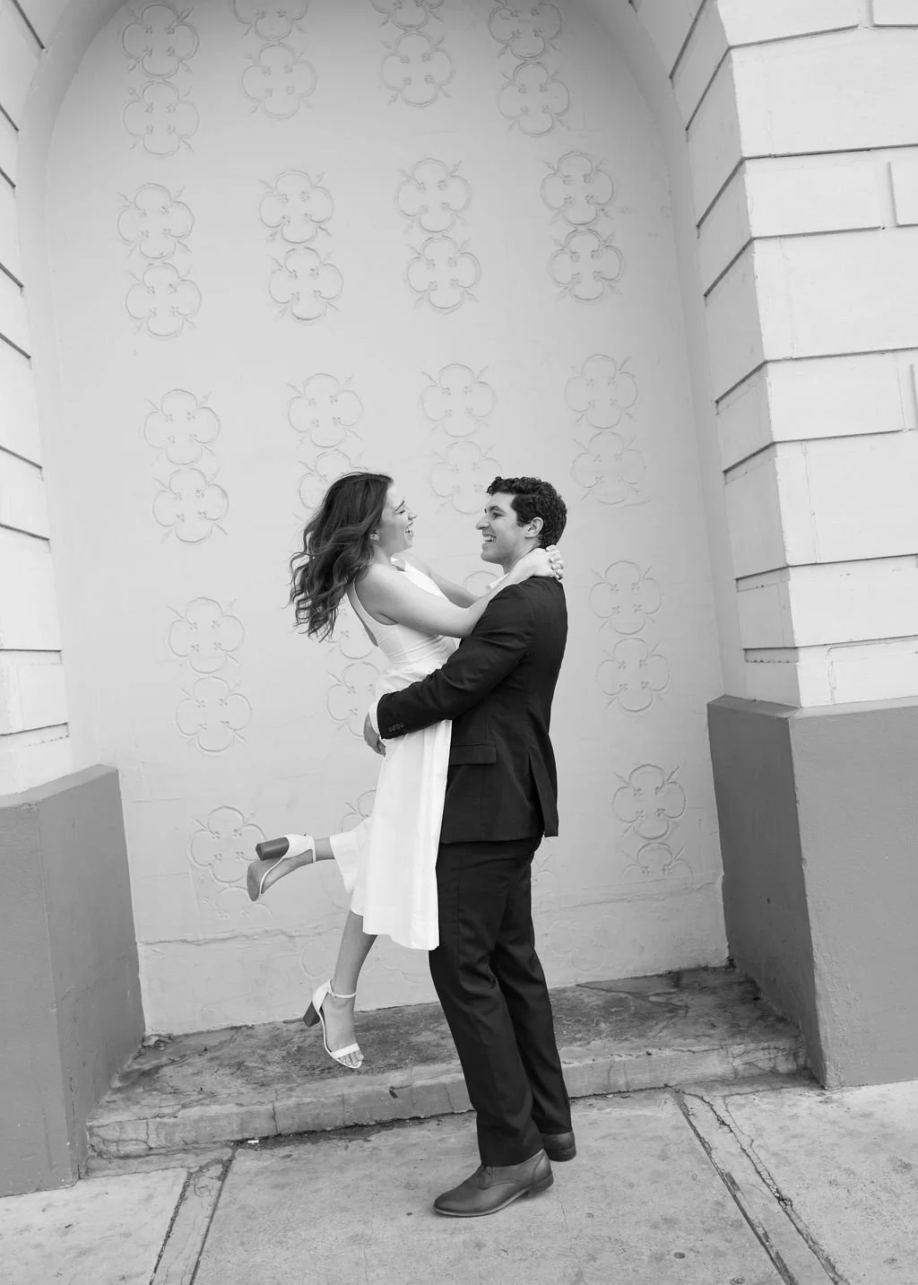 Couple laughing together in black and white in front of arched wall during engagement photos San Antonio.