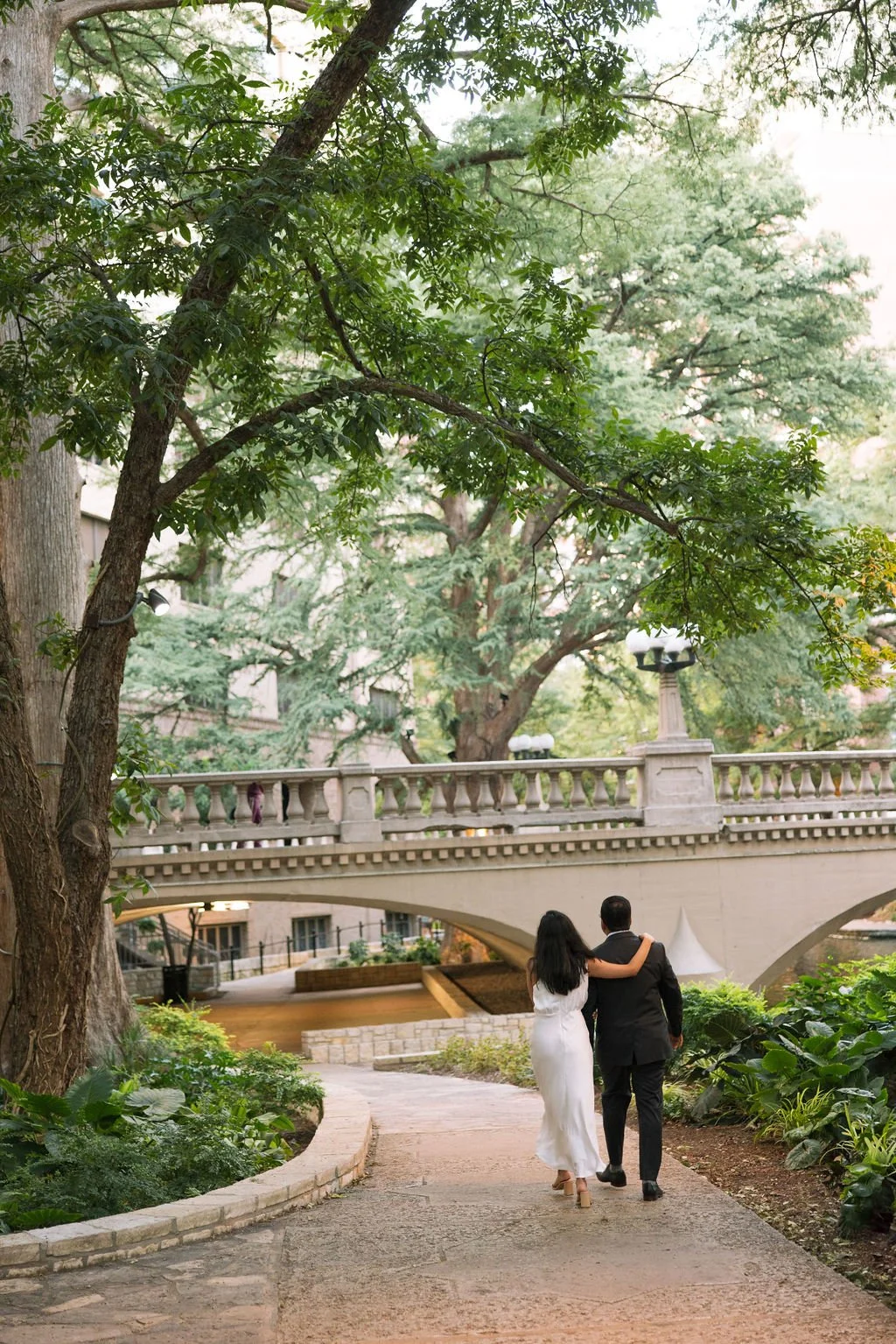 Couple walking hand in hand under bridge surrounded by trees during engagement photos San Antonio.