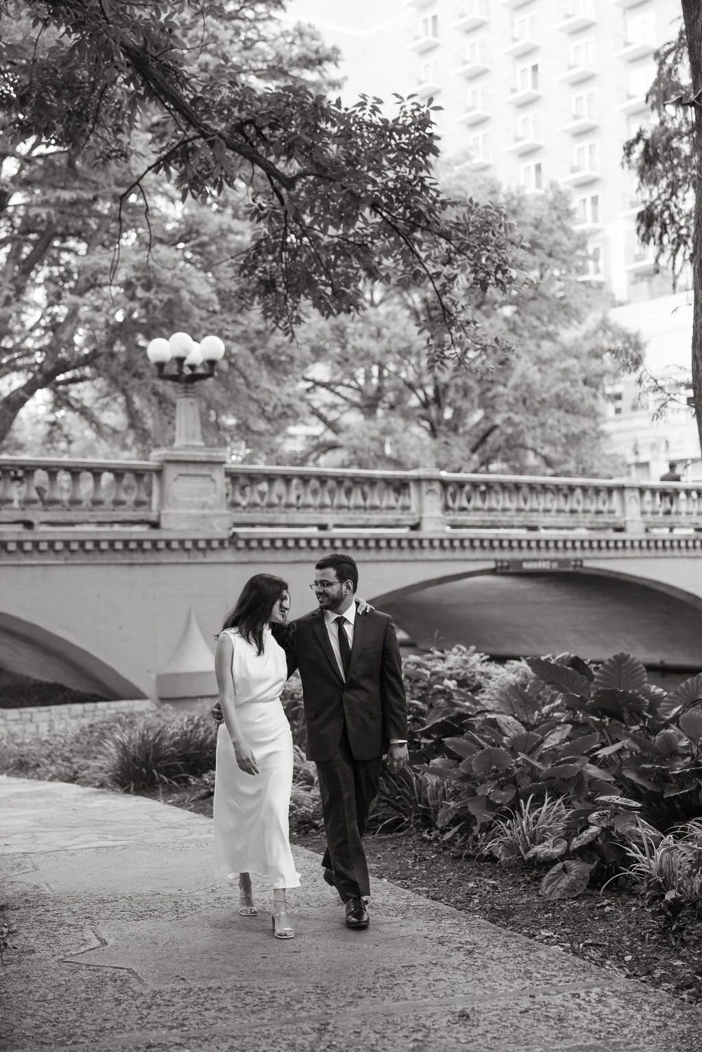 Couple walking in black and white on River Walk bridge during San Antonio engagement photos.