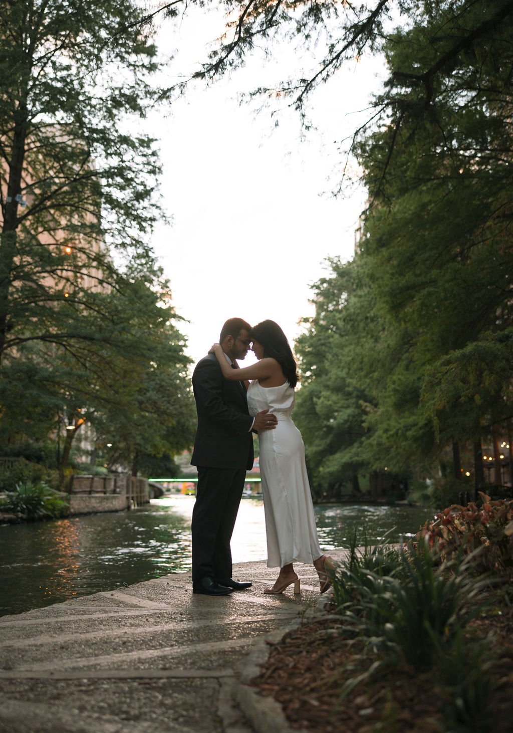 Couple kissing by riverfront during their San Antonio River Walk engaegment photos.
