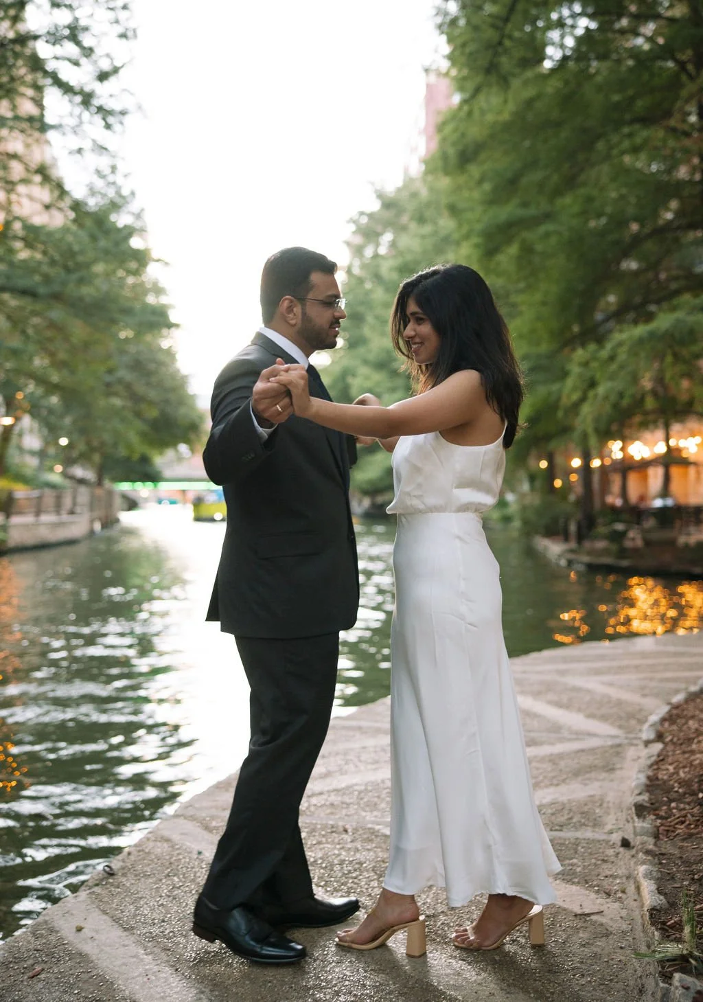 Couple dancing beside riverbank during San Antonio River Walk engagement photos.