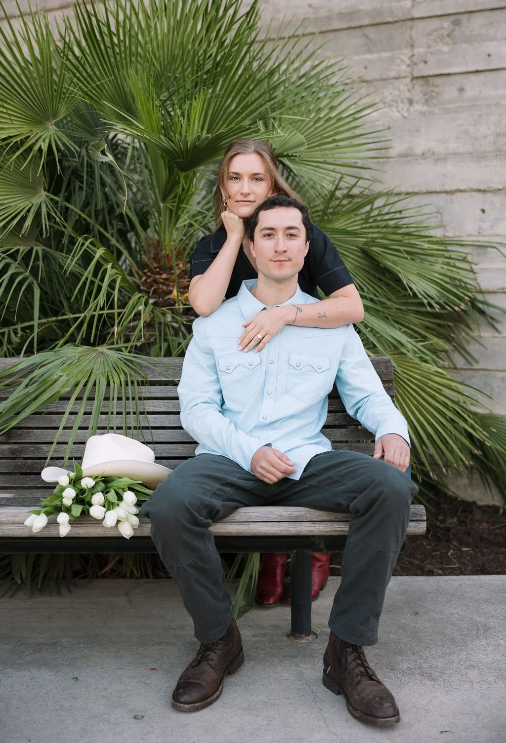 Couple hanging out on a park bench in front of some palm plants at the Pearl