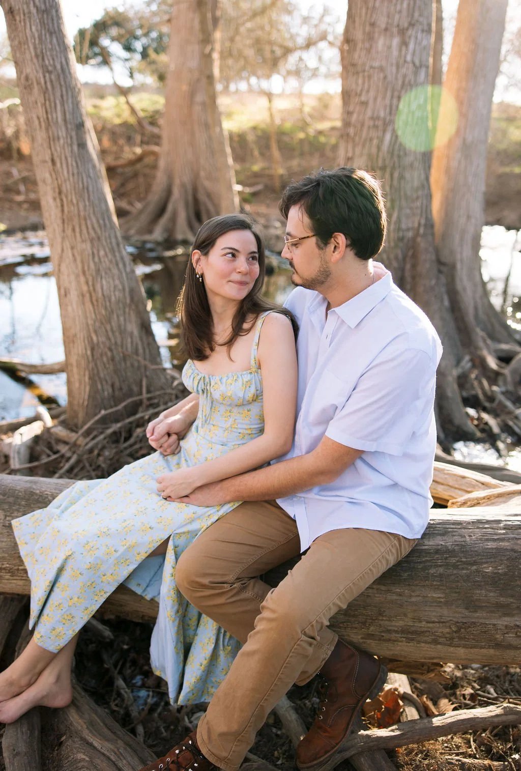 Couple sitting together on tree roots by water during San Antonio engagement photos.