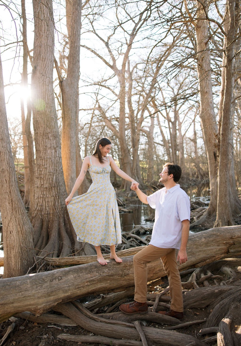 Couple sitting close together on log surrounded by trees during San Antonio engagement session.