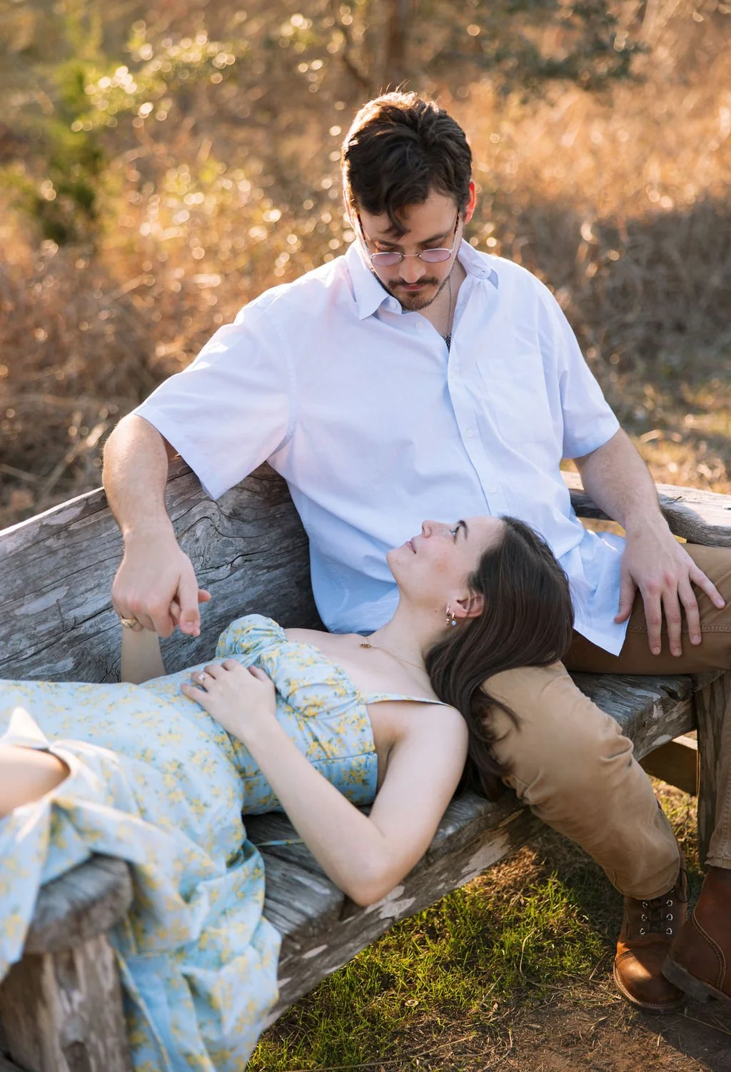 Couple sitting close together on log surrounded by trees during San Antonio engagement session.