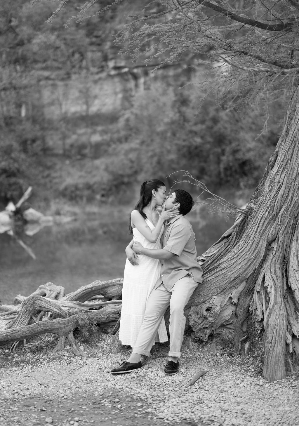 Couple kissing on tree roots in black and white at Guadalupe River State Park San Antonio engagement session.