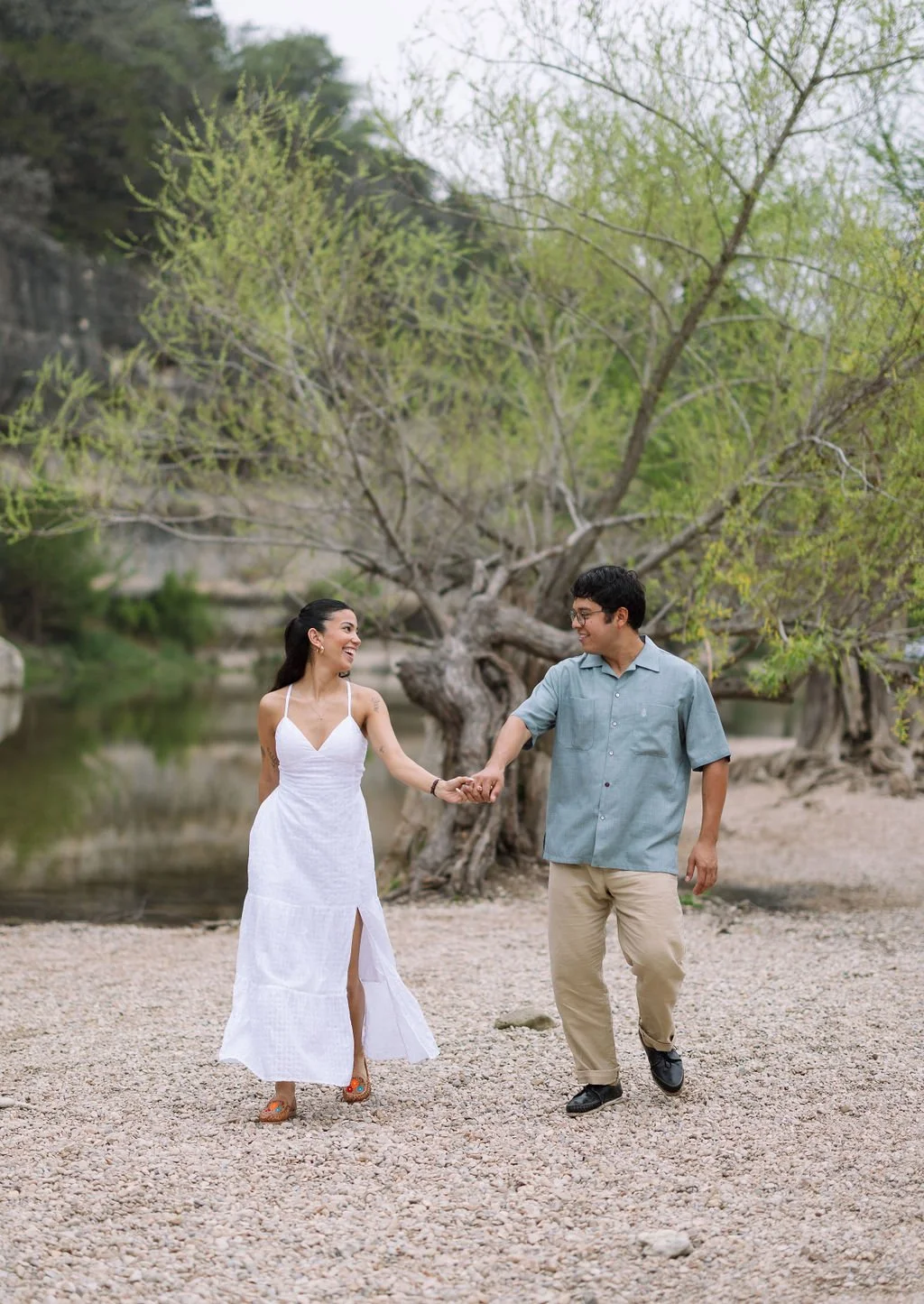Couple walking hand in hand along rocky shore during San Antonio engagement photos at Guadalupe River.