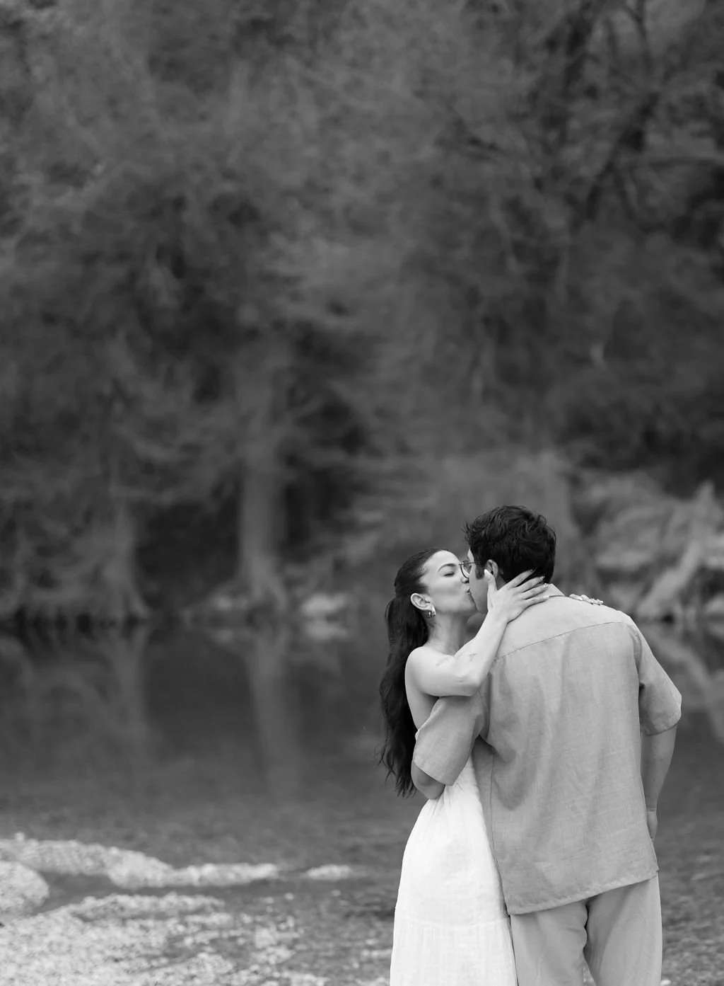 Couple embracing in black and white on riverbank during San Antonio engagement photos.