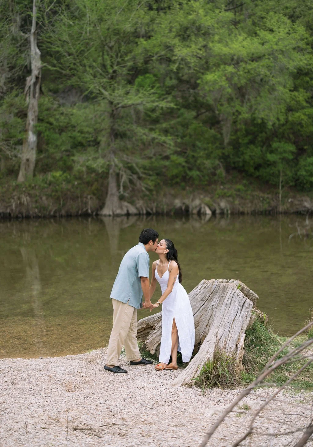 Couple kissing beside tree stump along riverbank during Guadalupe River State Park San Antonio engagement photos.