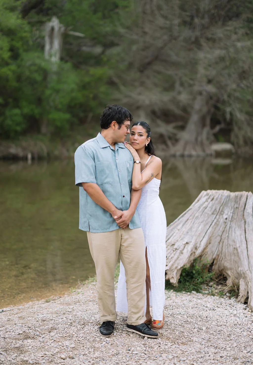 Couple cuddling together by tree stump during outdoor San Antonio engagement session.