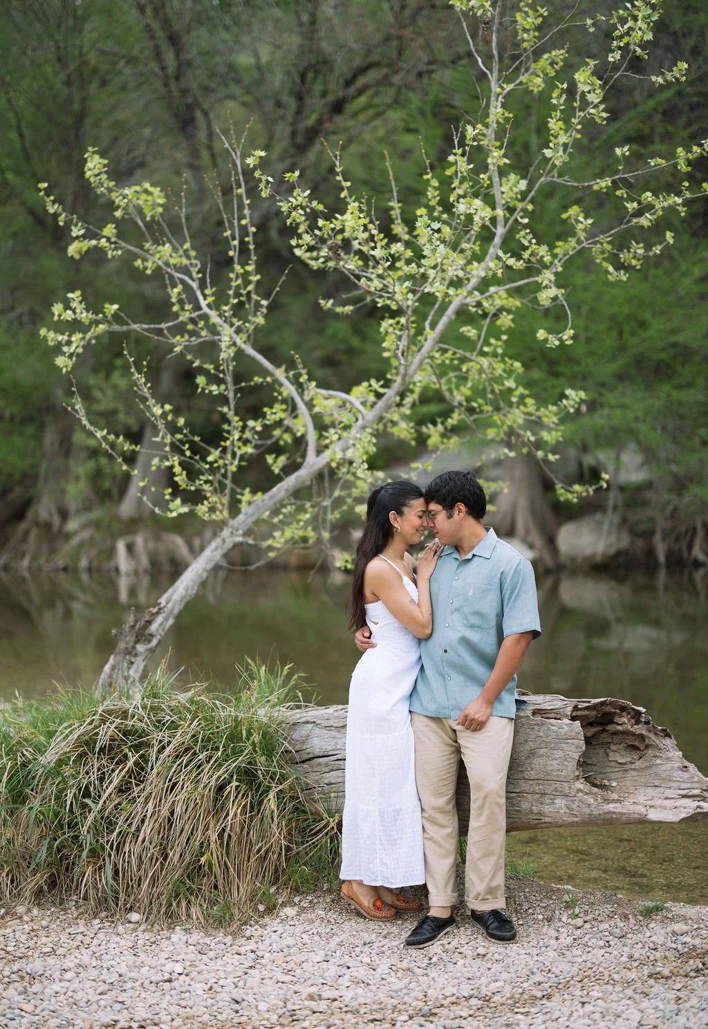Couple kissing under green tree along riverbank during Guadalupe River State Park engagement photos.