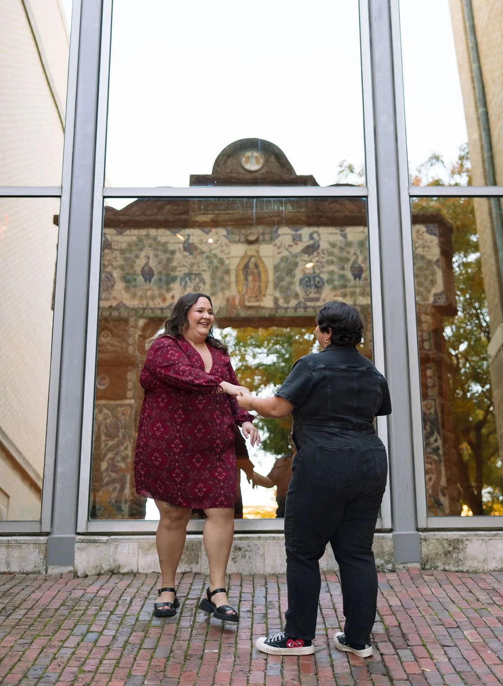 Couple holding hands in front of mural reflection window during San Antonio Museum of Art engagement session.