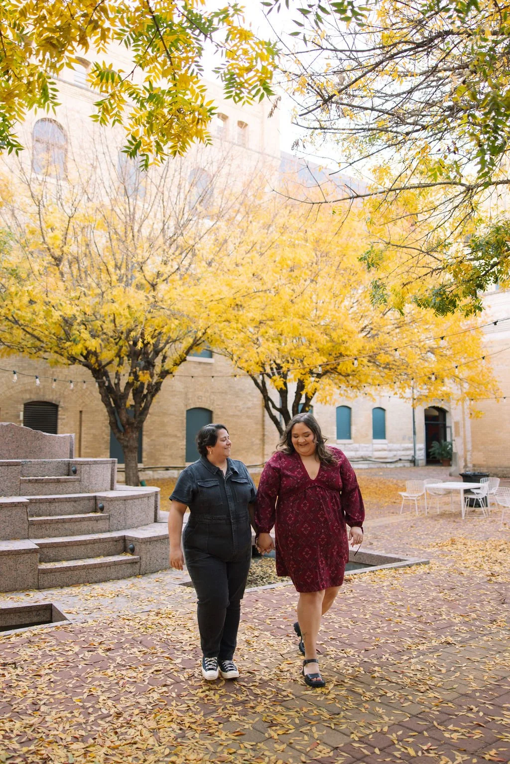 Couple walking through courtyard with fall leaves during San Antonio Museum of Art engagement photos.
