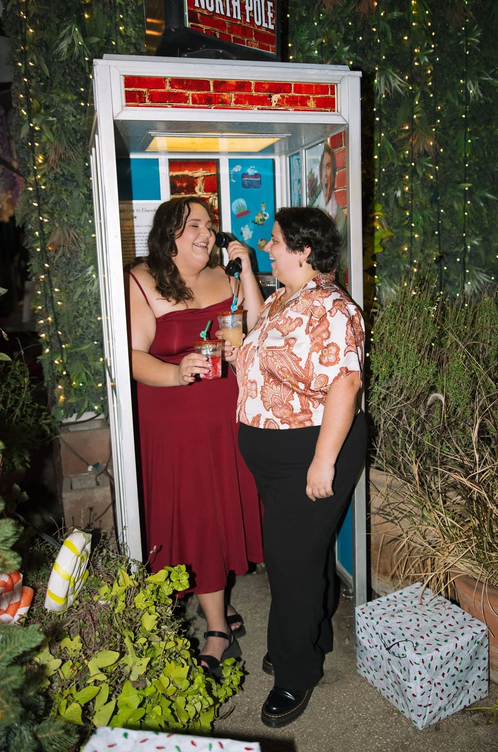 Couple laughing together by retro phone booth during Idle Beer Hall engagement session in San Antonio.