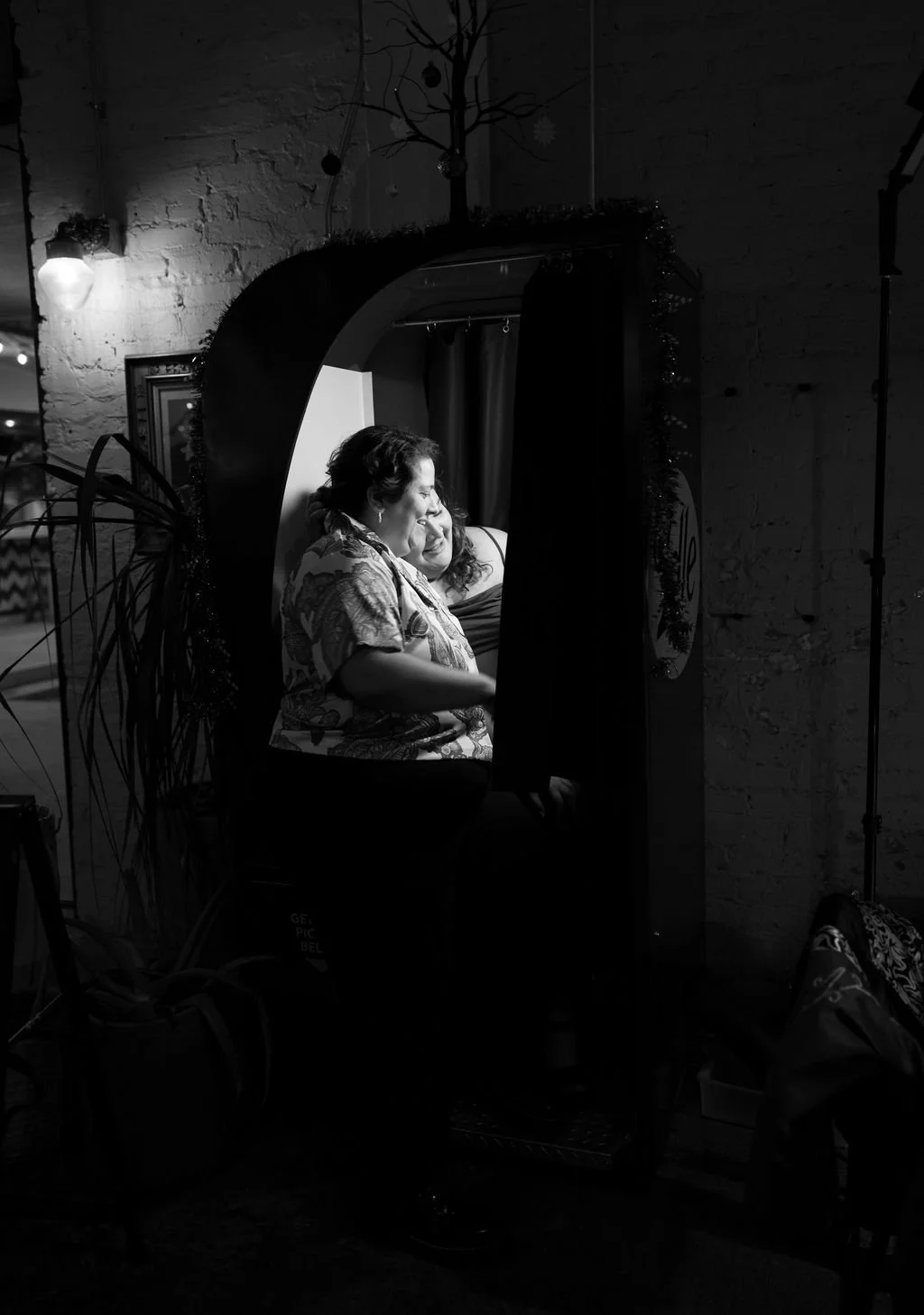 Couple sitting together in the photobooth in a moody black and white candid engagement photo.