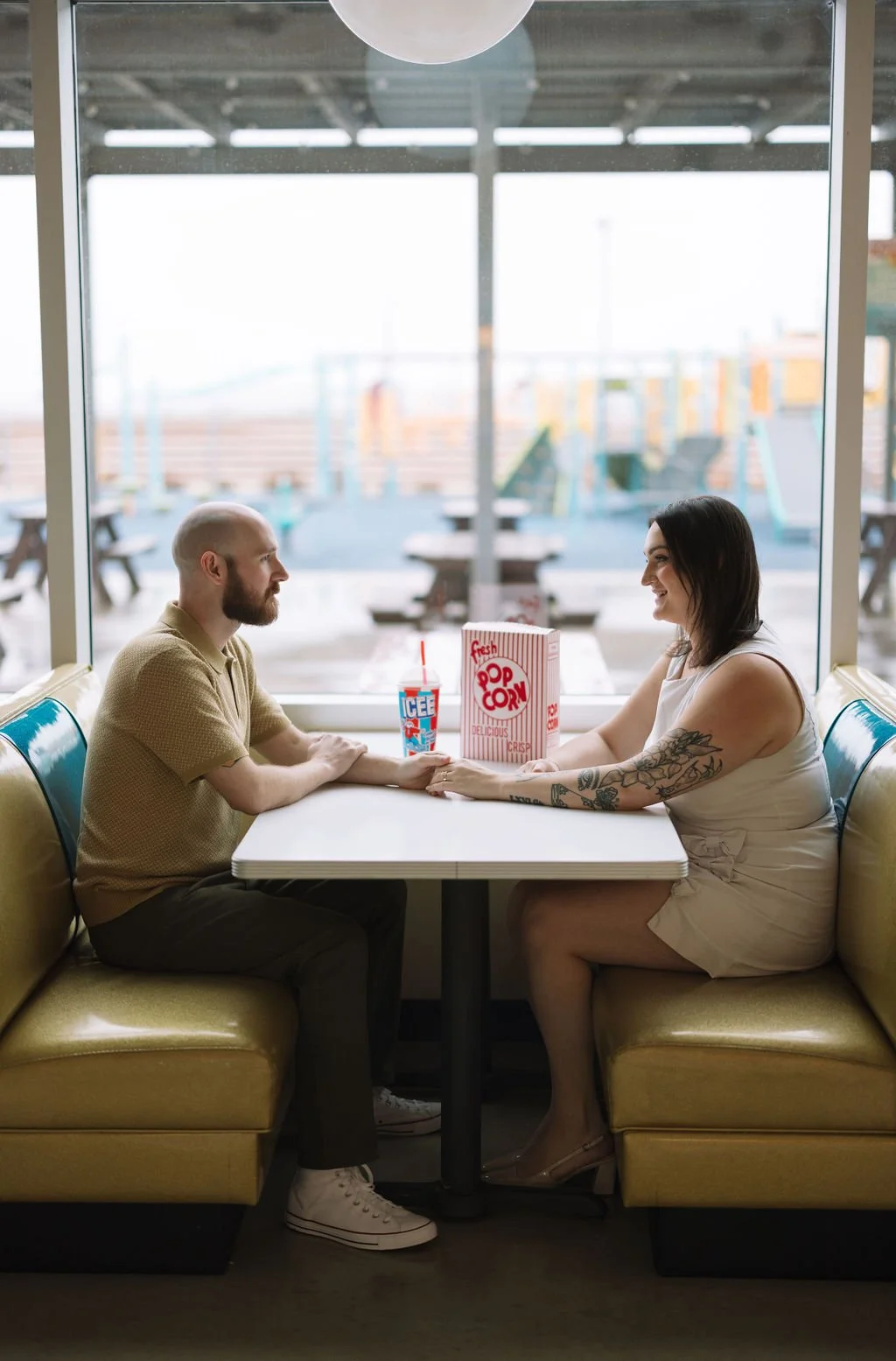 Couple sitting at retro diner booth with popcorn during Stars &amp; Stripes Drive-In San Antonio engagement photos.